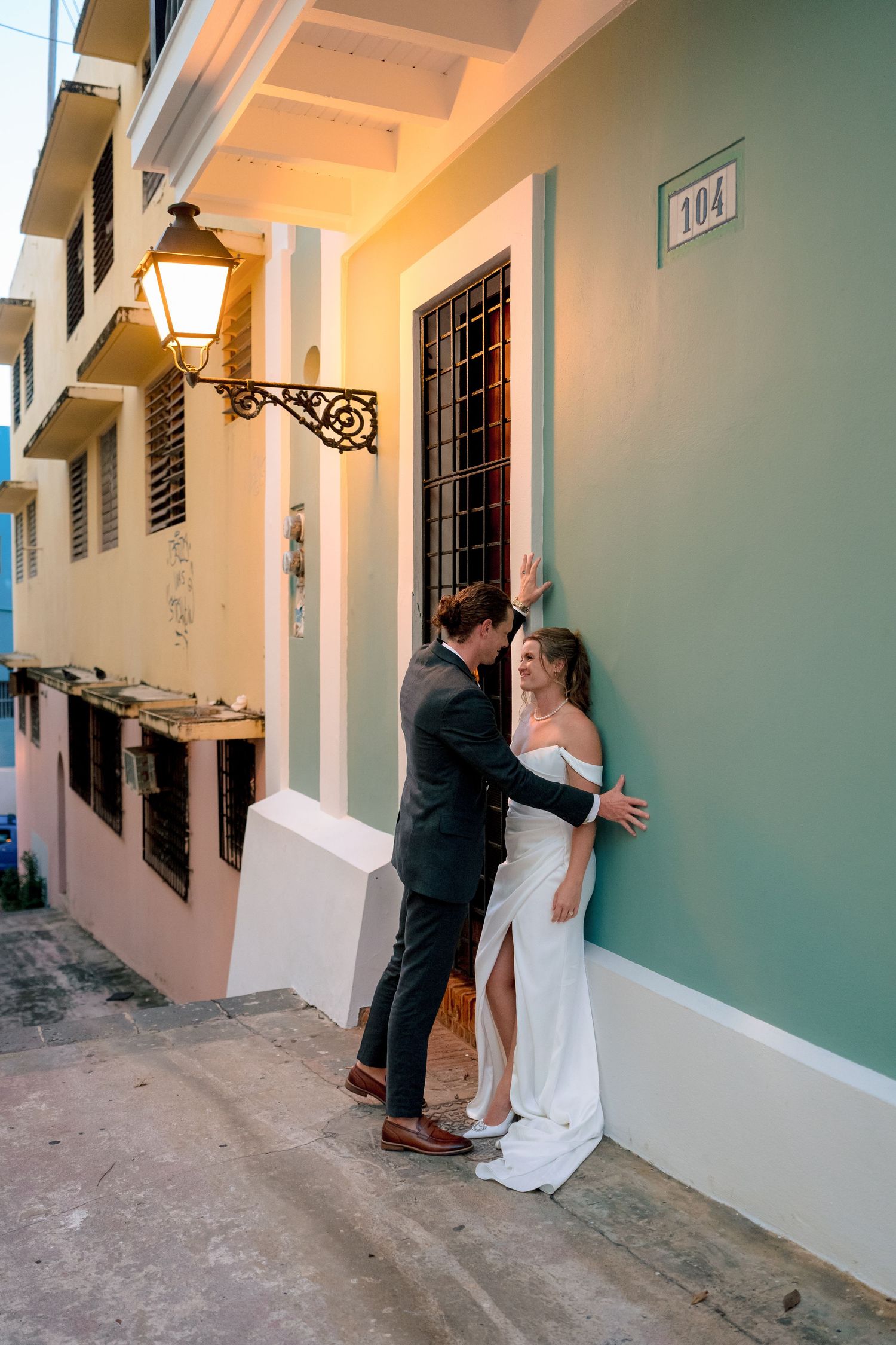 Wedding couple sharing romantic moment against teal building wall on charming Old San Juan cobblestone street at dusk.