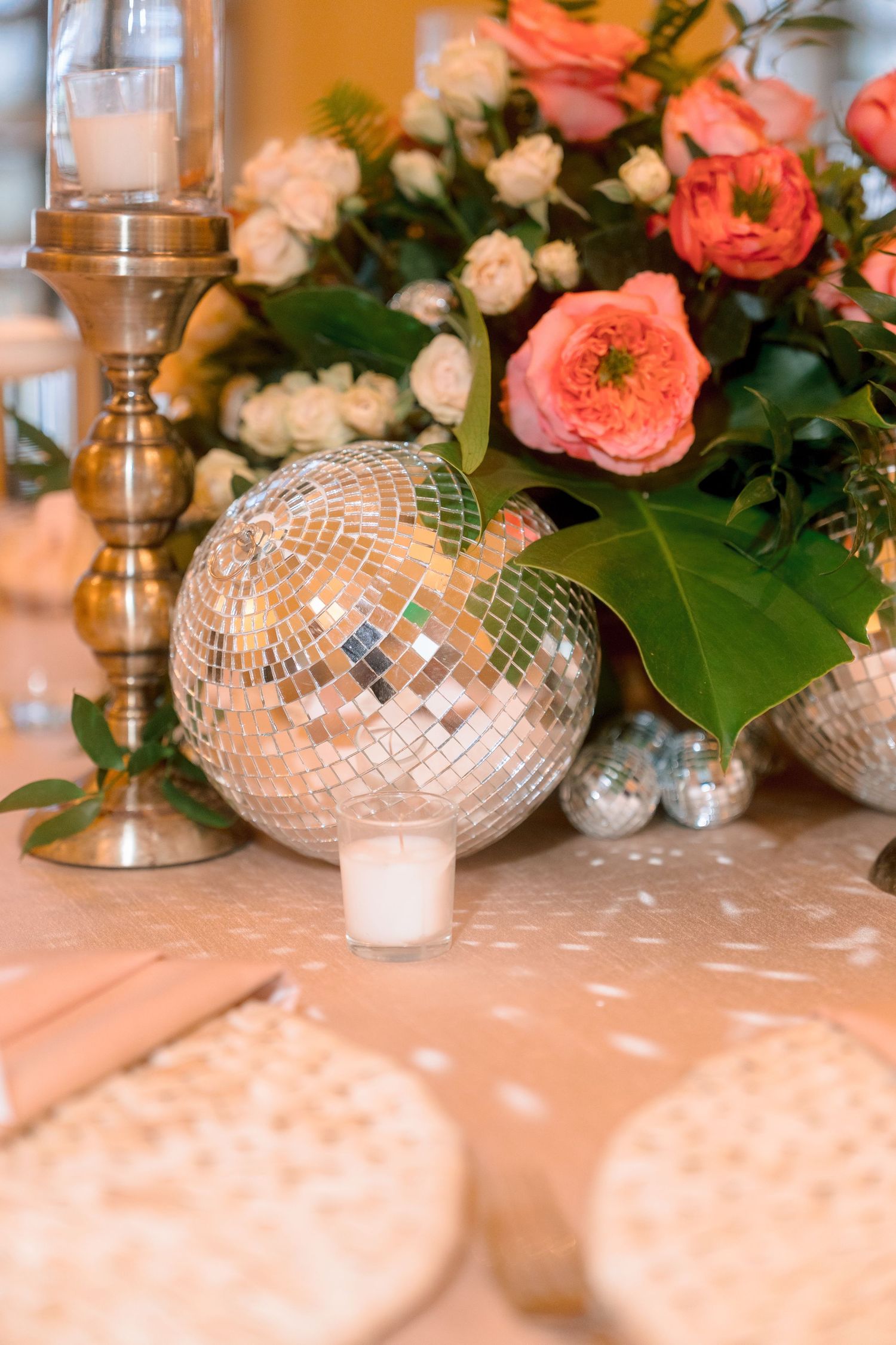 Elegant wedding table centerpiece with a mirrored disco ball, pink roses, white flowers, greenery, and a gold candlestick holder.