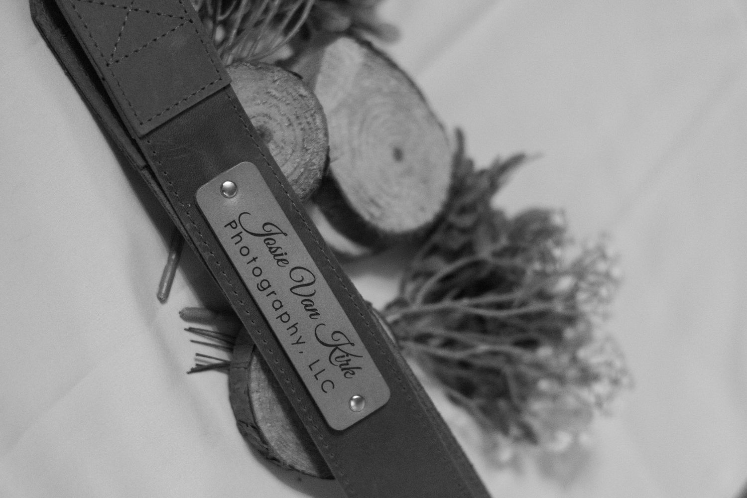 Black and white close-up of Jessie Van Kirk Photography LLC engraved leather camera strap.