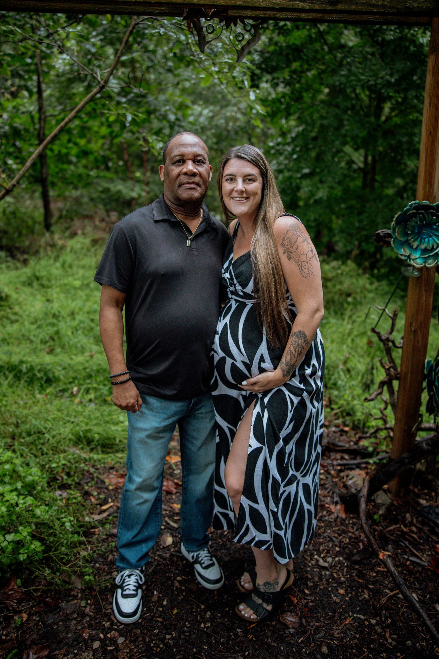 A smiling couple poses together in a lush garden setting, the woman wearing a black and white floral dress.