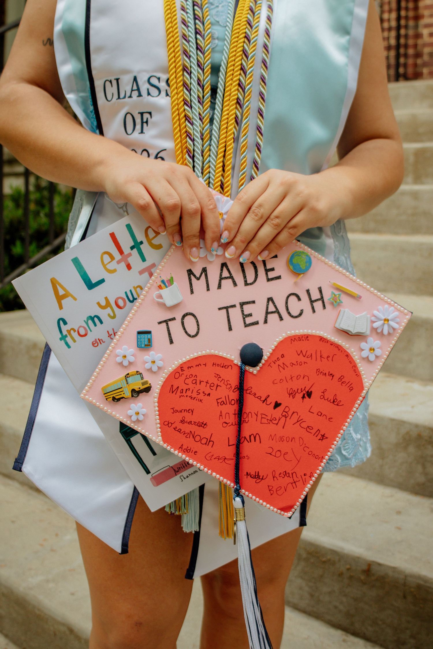 Graduate holds decorated mortarboard cap reading Made to Teach with Class of 2026 stole.