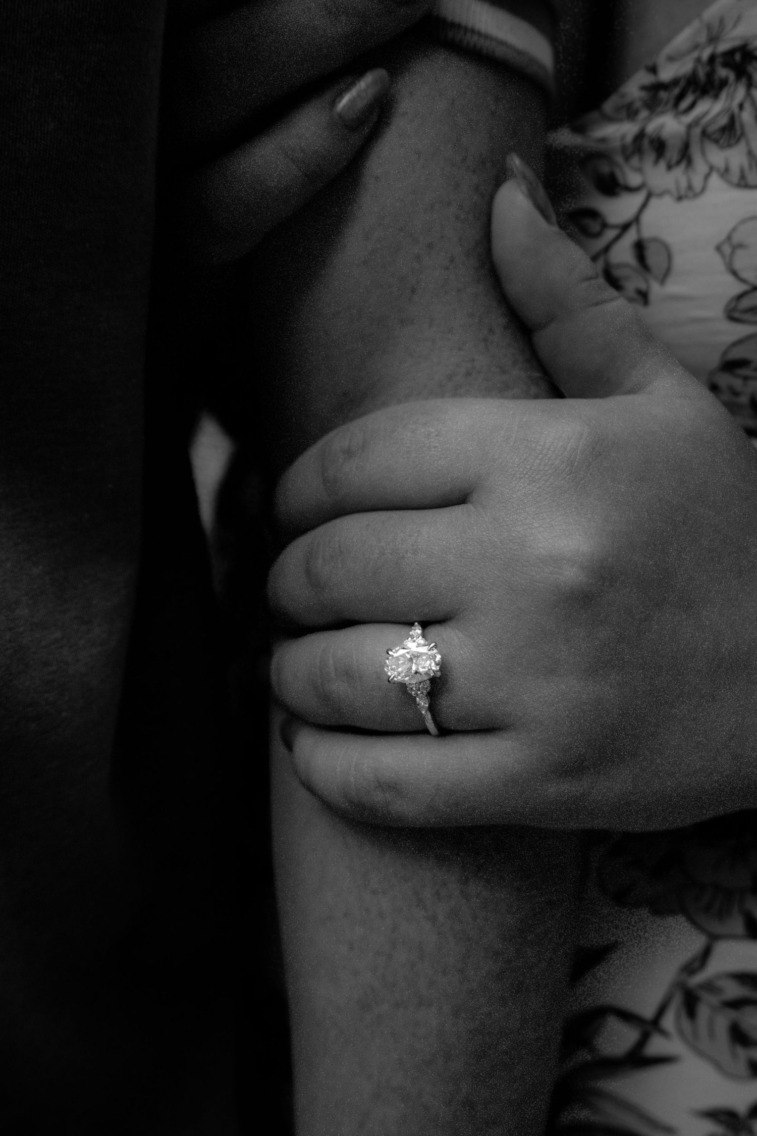 Close-up black and white photo of woman's hand with diamond engagement ring holding man's arm.