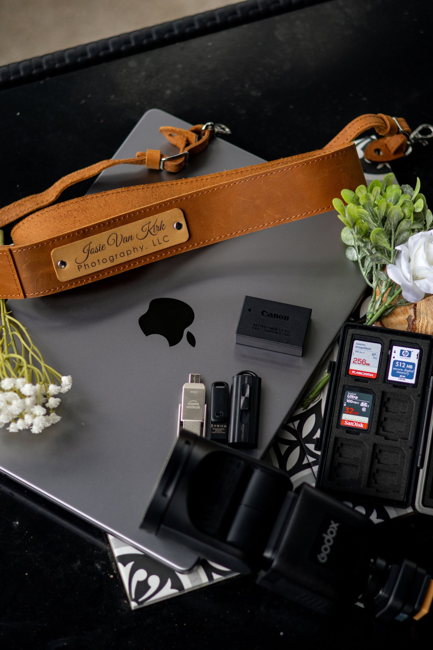 Flat lay of photography gear including Canon camera, MacBook, SD cards, and leather strap.