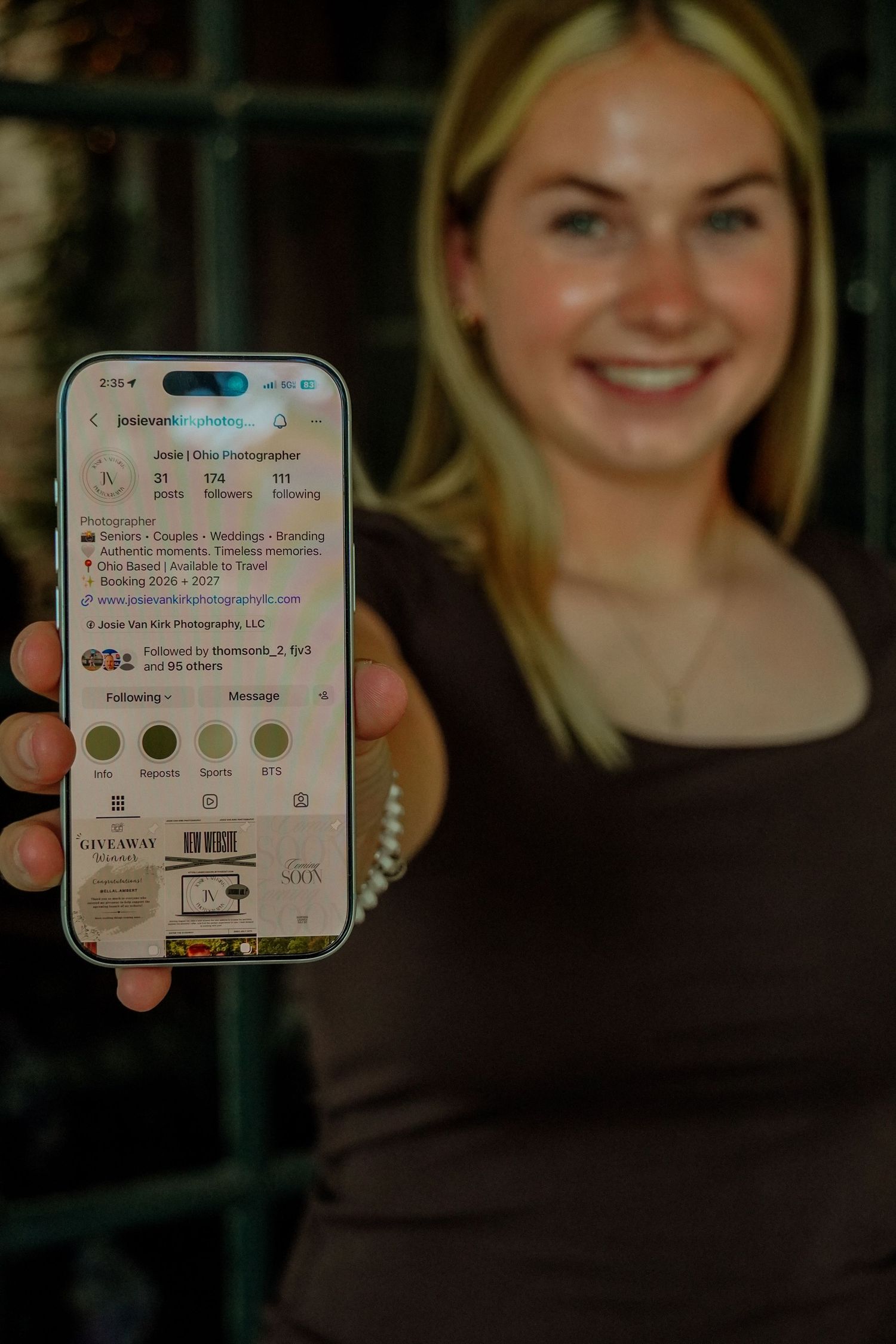 Smiling blonde woman holding up smartphone showing Instagram photography profile page.
