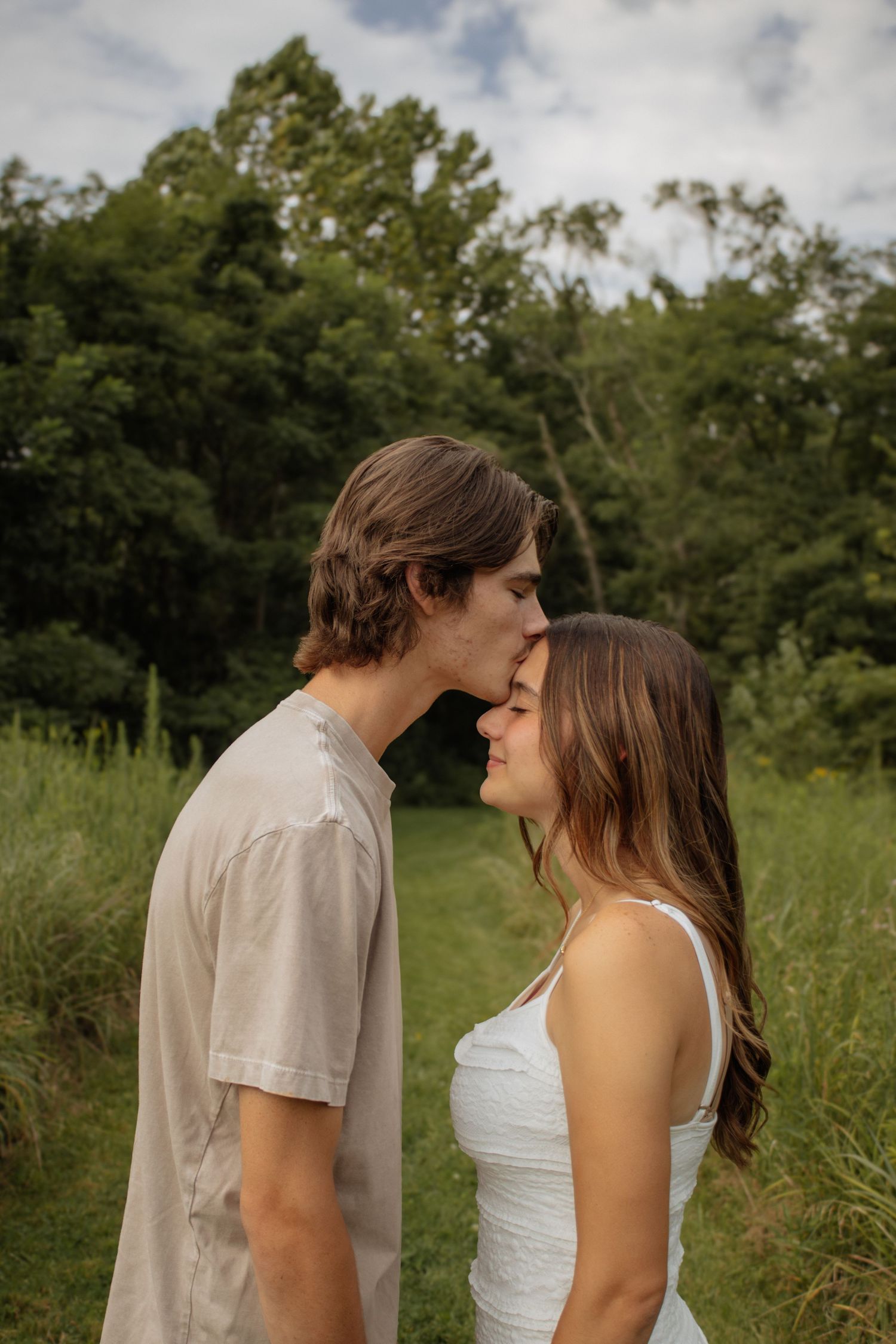 A young couple sharing a tender nose kiss in a lush green meadow, the woman in white dress and man in beige shirt.