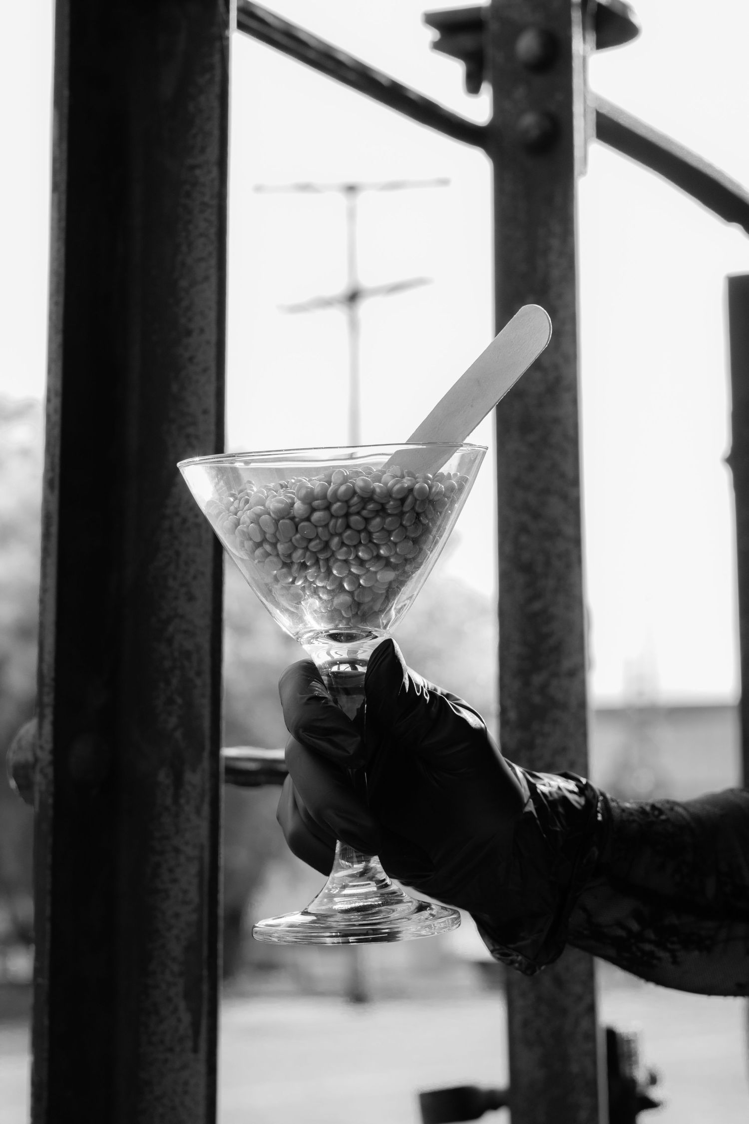Black and white photo of gloved hand holding martini glass filled with pearl candies outdoors.