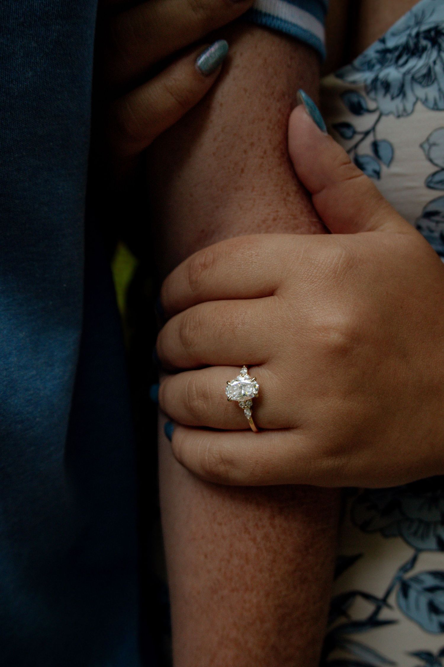 Close-up of woman's hand holding man's arm, showcasing a sparkling diamond engagement ring.