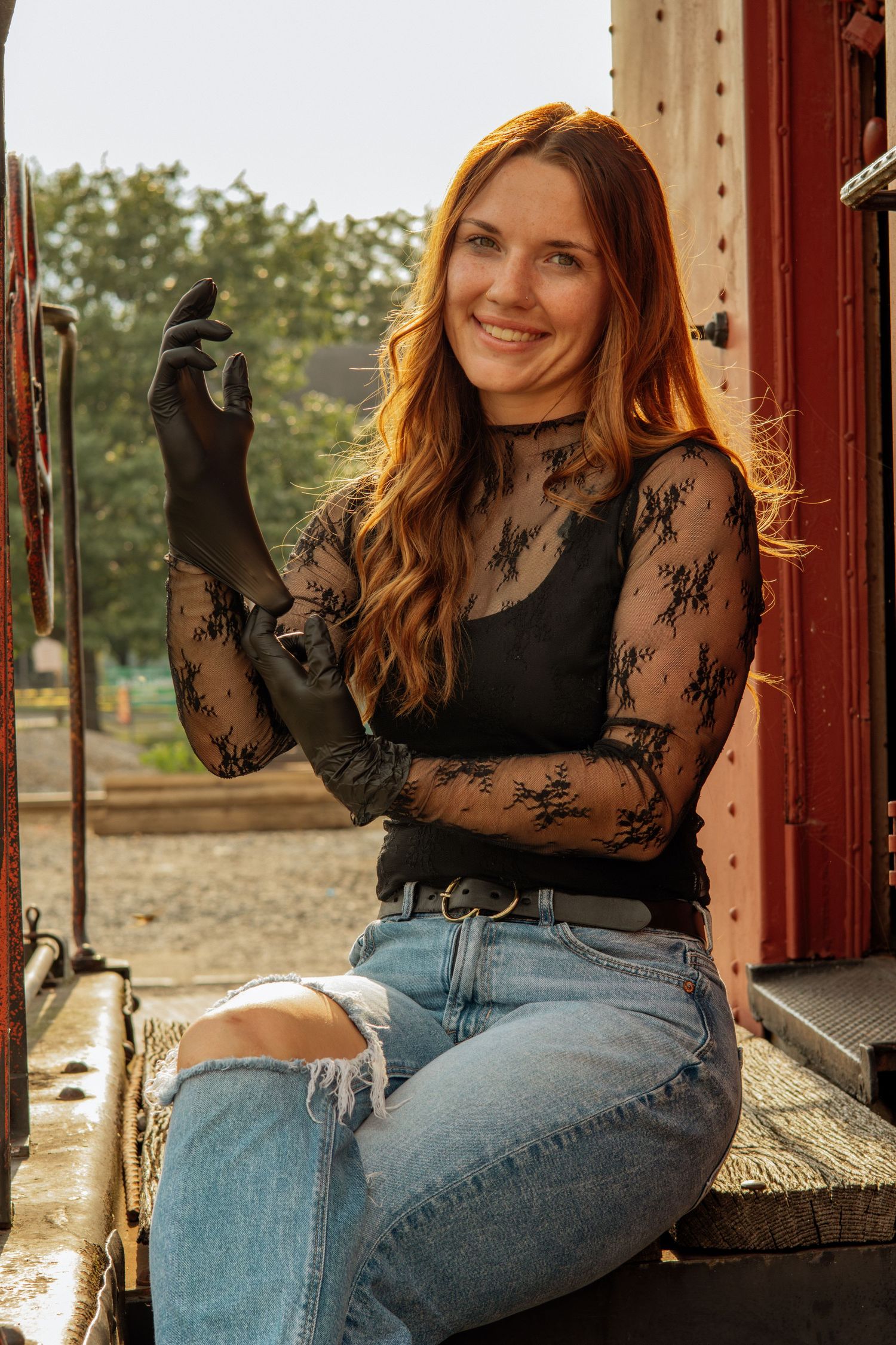 Smiling redhead woman in black lace top and ripped jeans sitting outdoors.