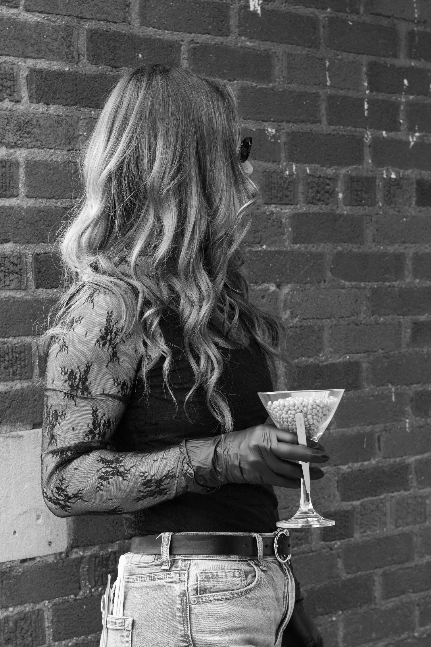 Black and white photo of blonde woman in lace top holding martini glass against brick wall.