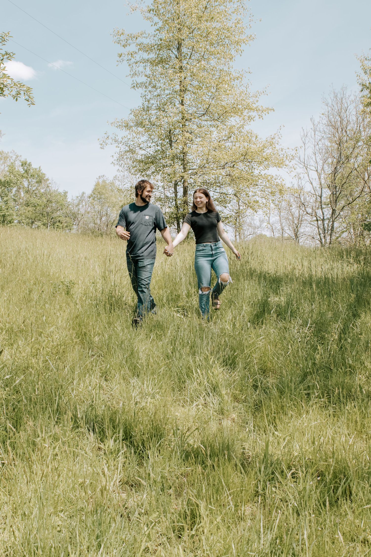 A joyful couple holds hands while walking through a lush green meadow on a sunny day.