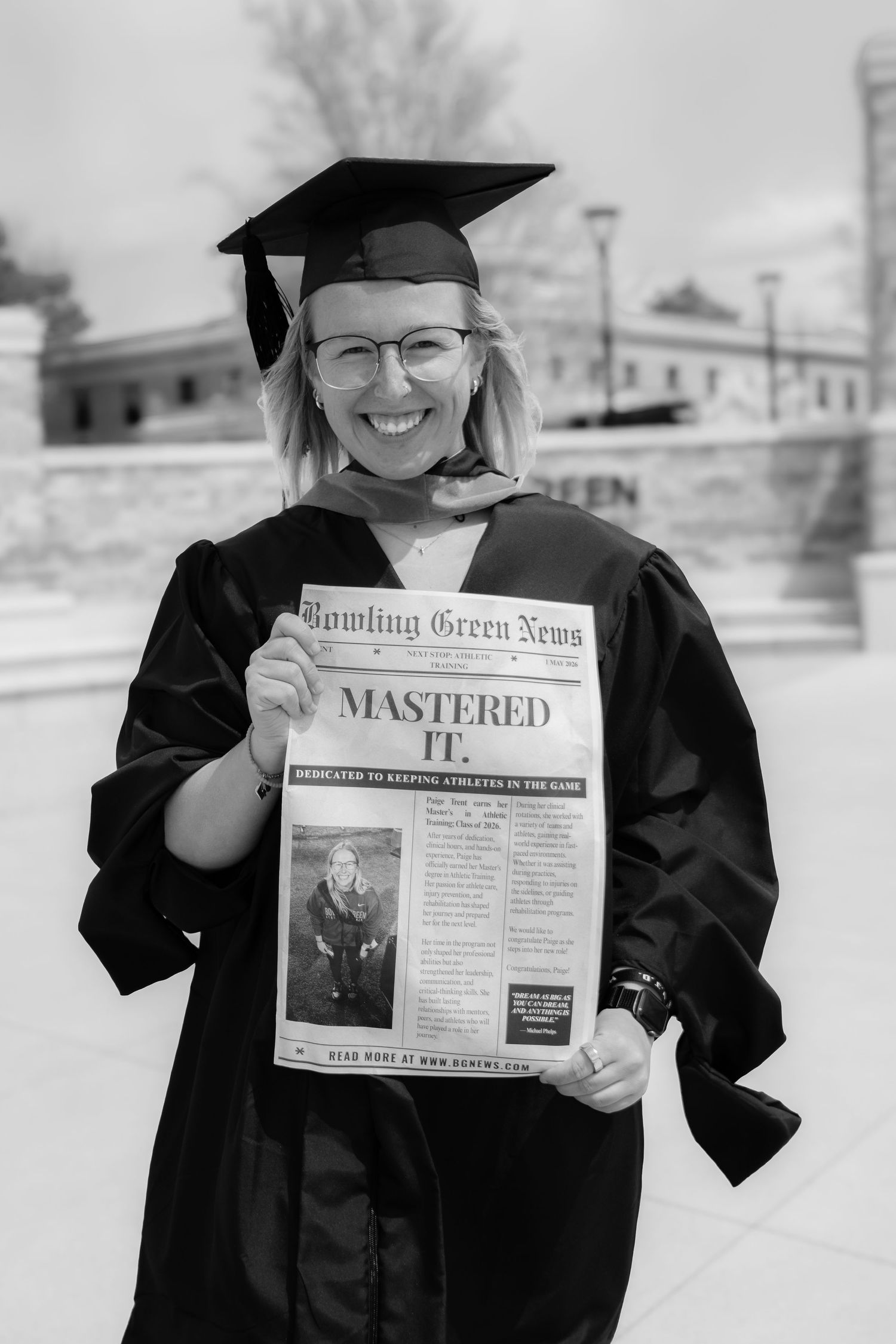Graduate in cap and gown holding Bowling Green News newspaper with headline Mastered It in black and white.