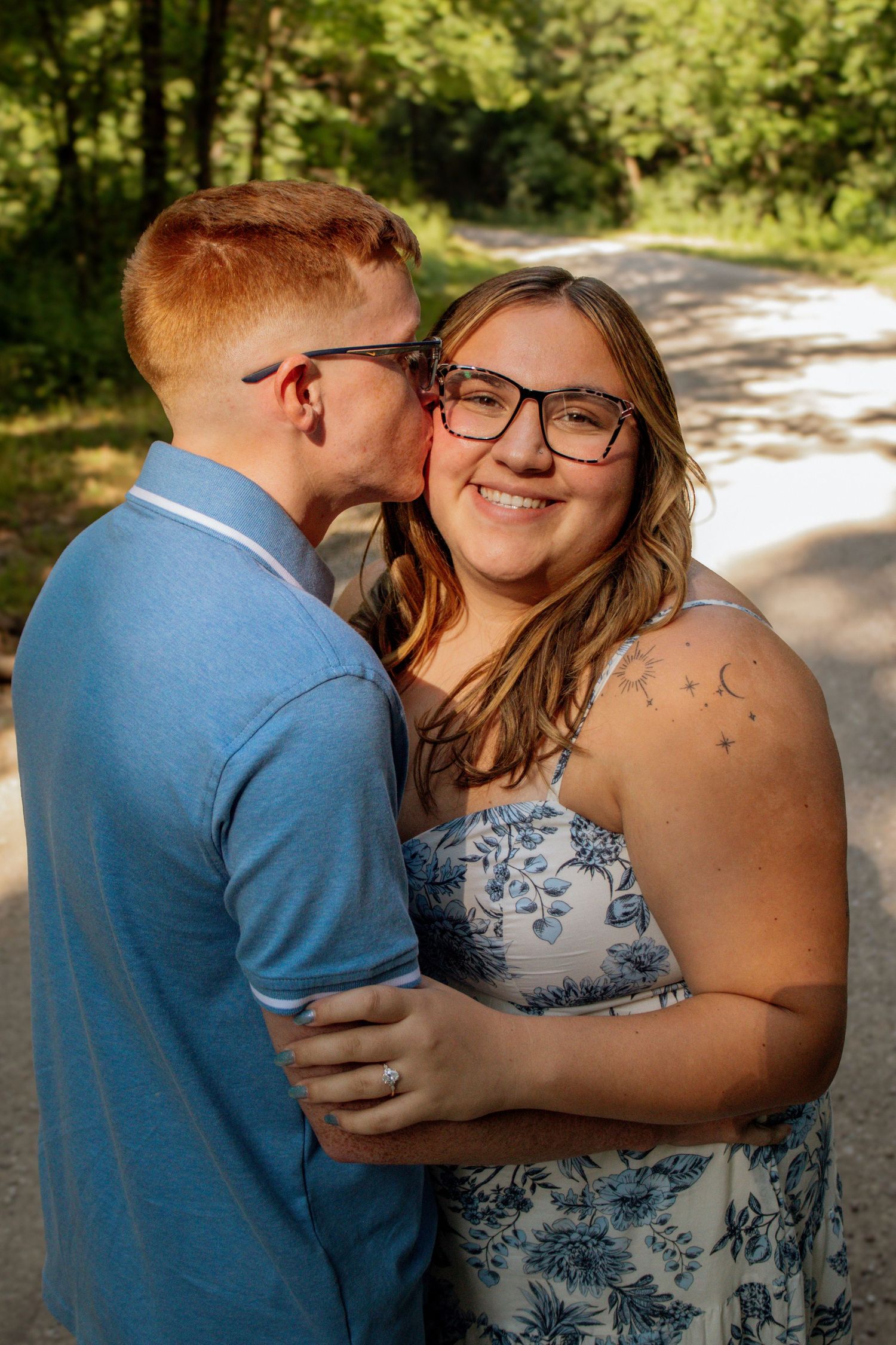 A happy couple shares a tender kiss on a tree-lined gravel path in summer.