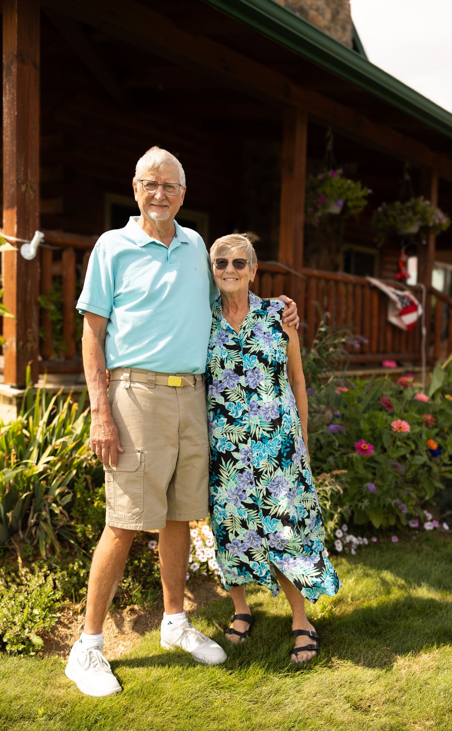 Elderly couple smiling together in a garden outside a log home on a sunny day.