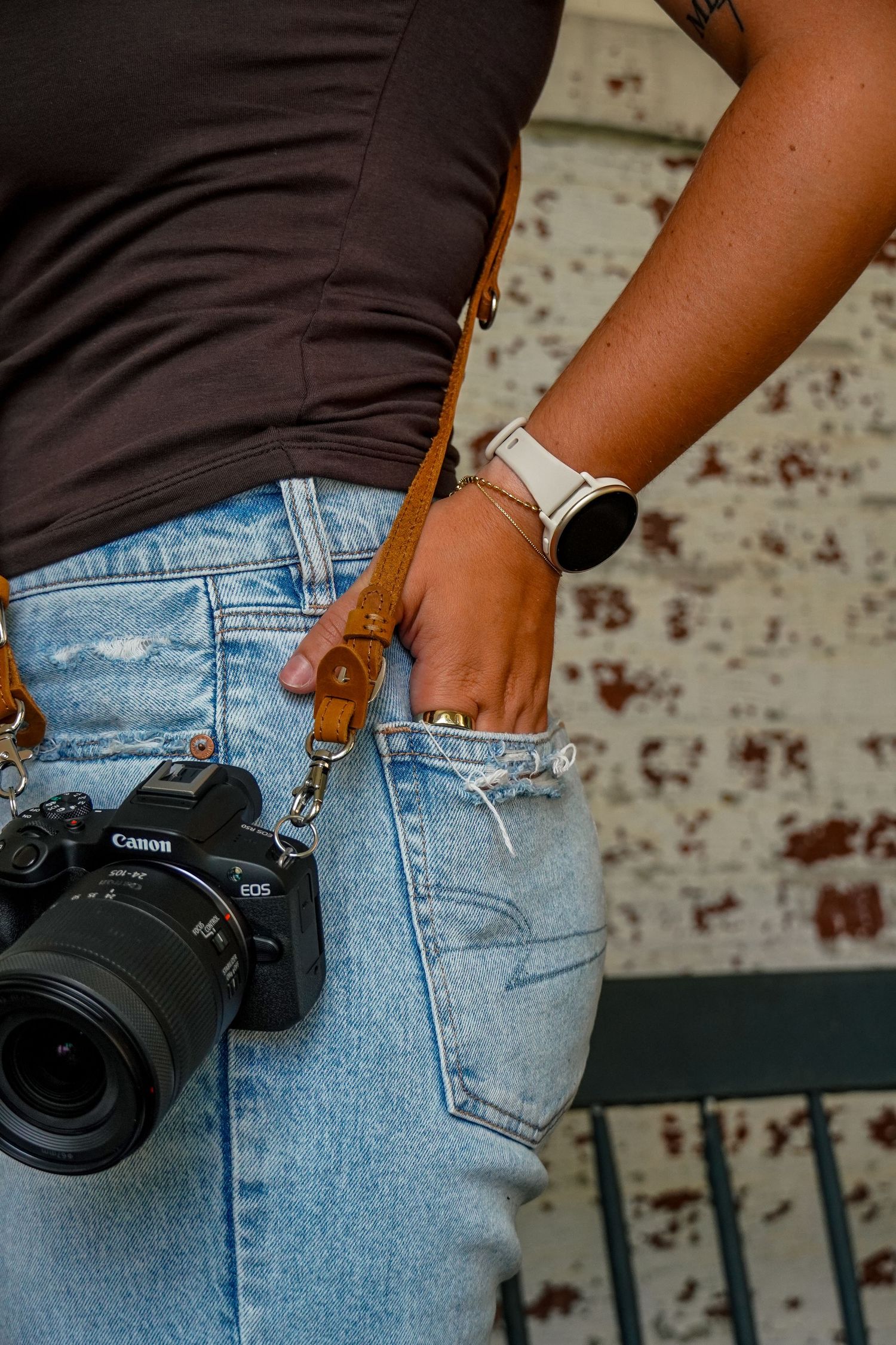 Canon EOS camera hanging from tan leather Jessie Van Kirk Photography strap on photographer in jeans.
