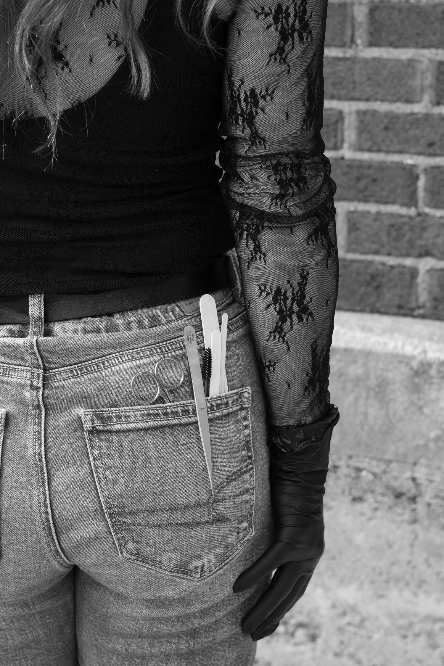 Black and white photo of woman in lace sleeves with scissors in back jeans pocket.