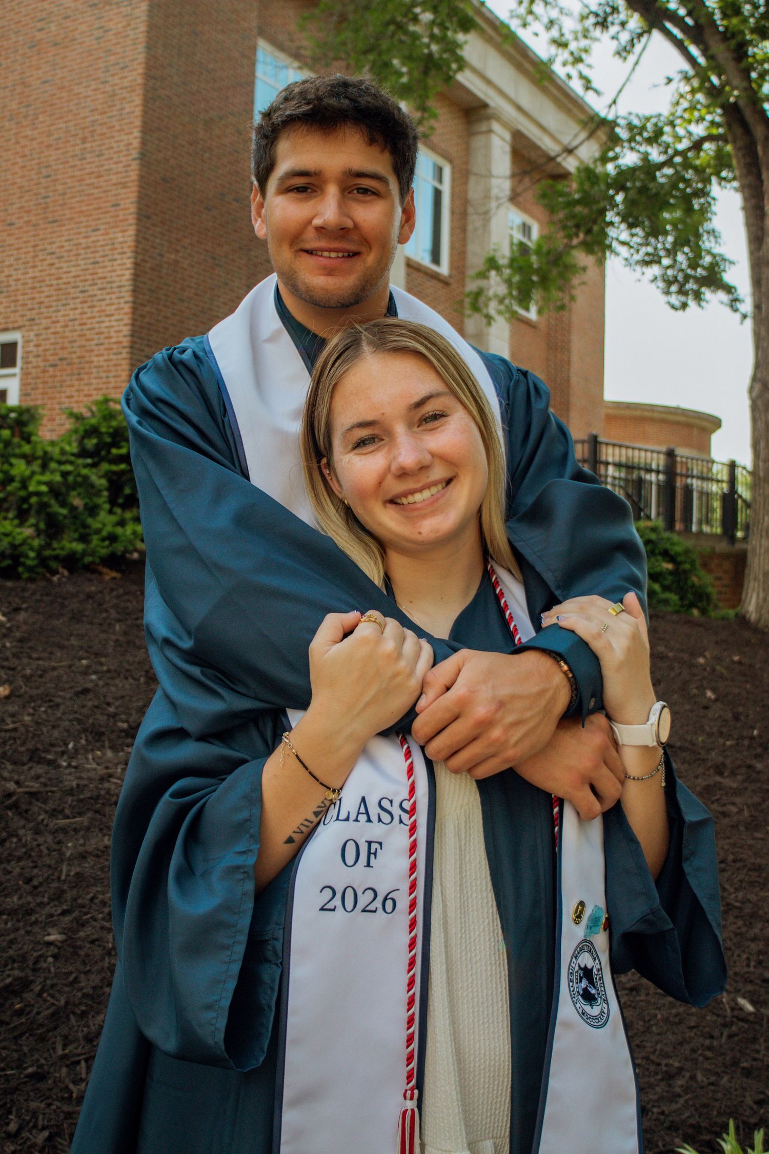 Two graduates in teal gowns embracing and smiling at Class of 2026 ceremony.