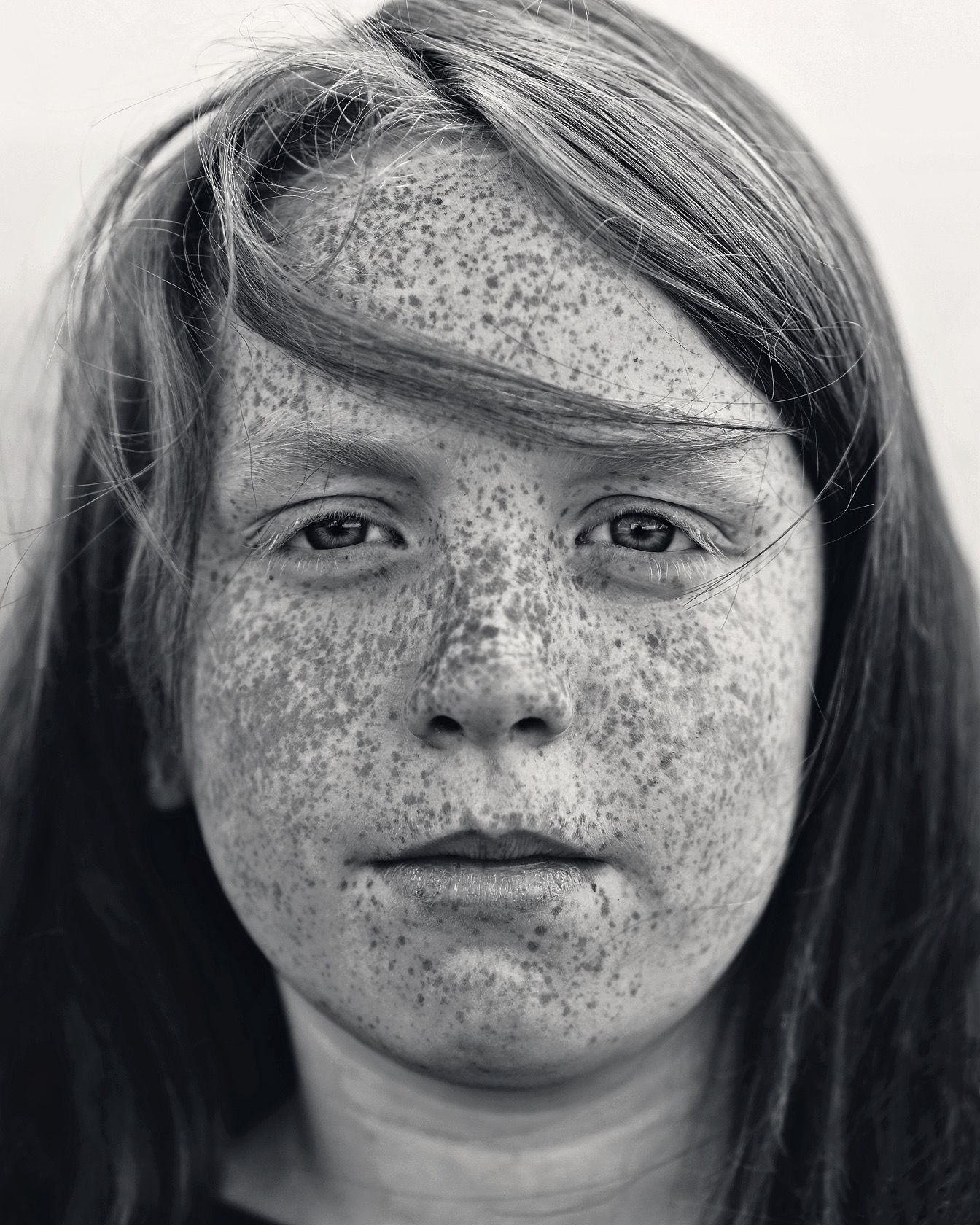 Detailed black and white close-up portrait of freckled child with long hair facing camera.