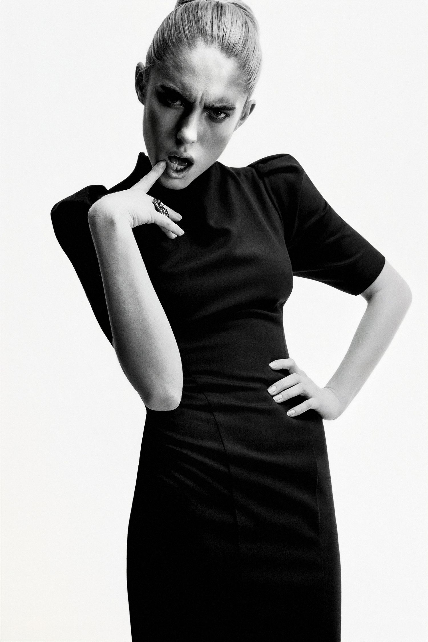 Black and white fashion photo of a woman in a sleek black dress with dramatic makeup, posing confidently.