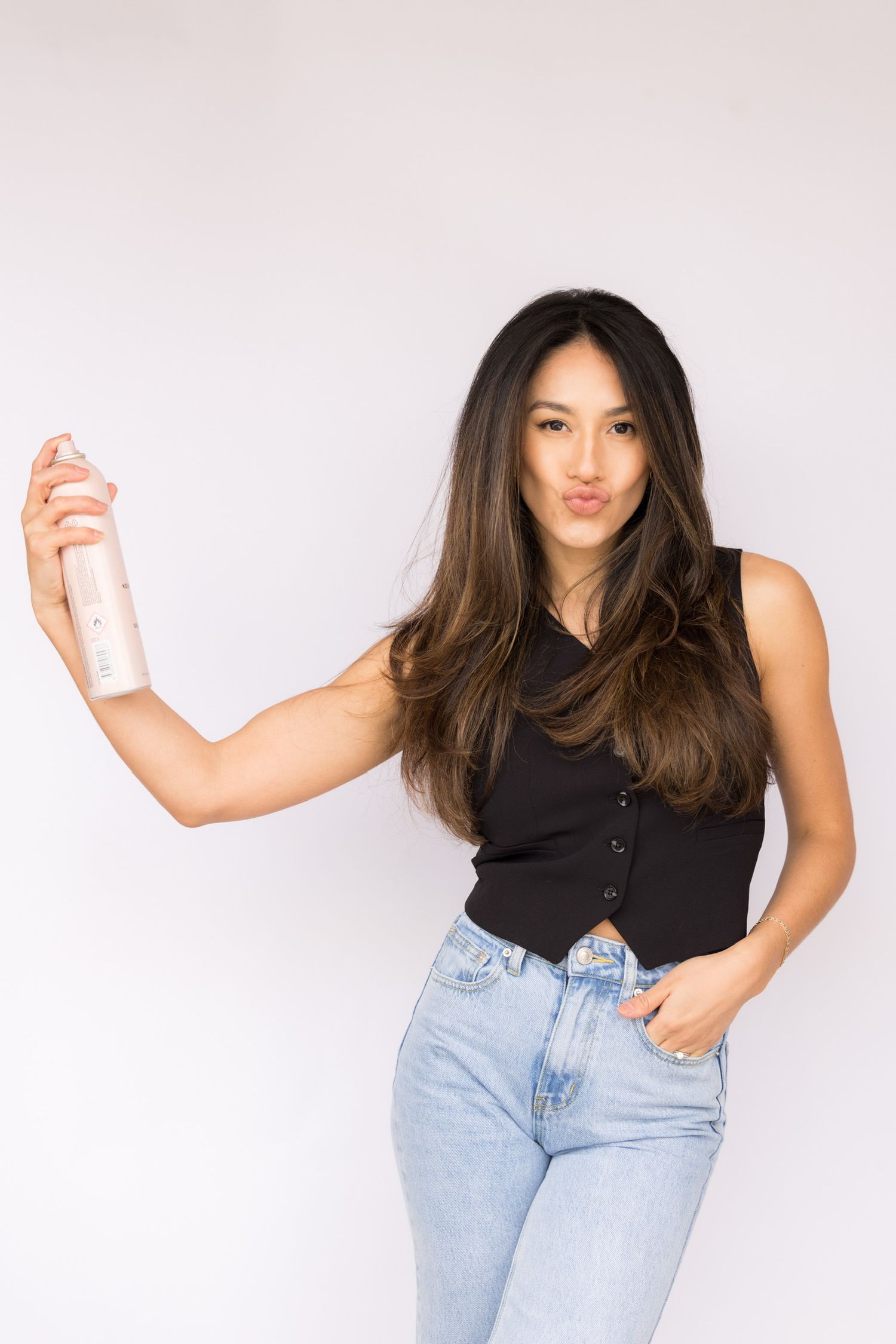 Woman in black sleeveless top holding hair spray can in studio.