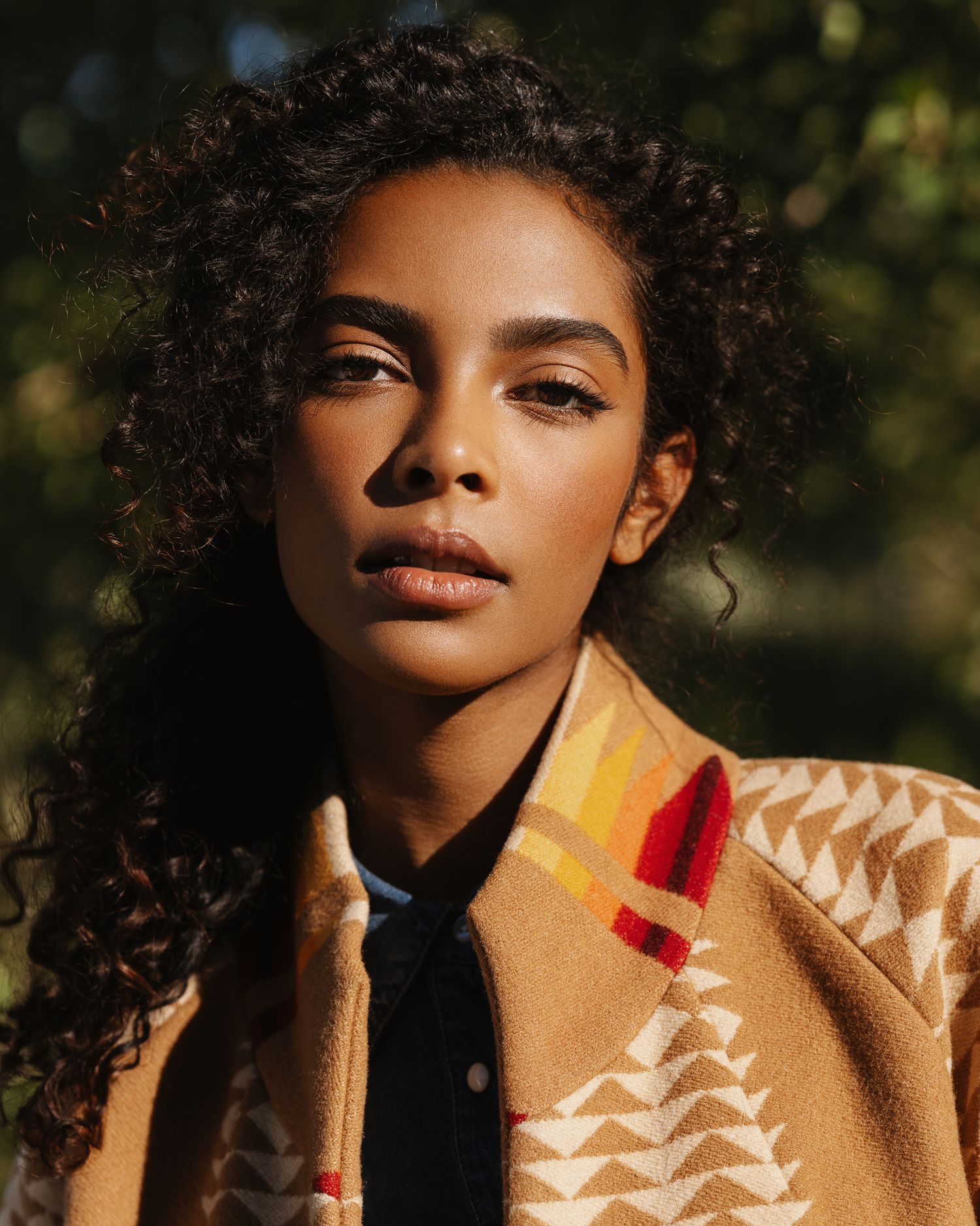 Woman with curly hair wearing a patterned Pendleton wool coat outdoors in warm sunlight.
