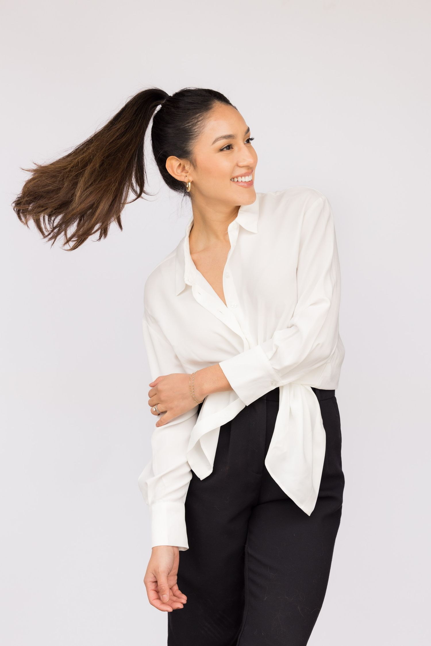 Smiling woman in white blouse and black pants with ponytail swinging.