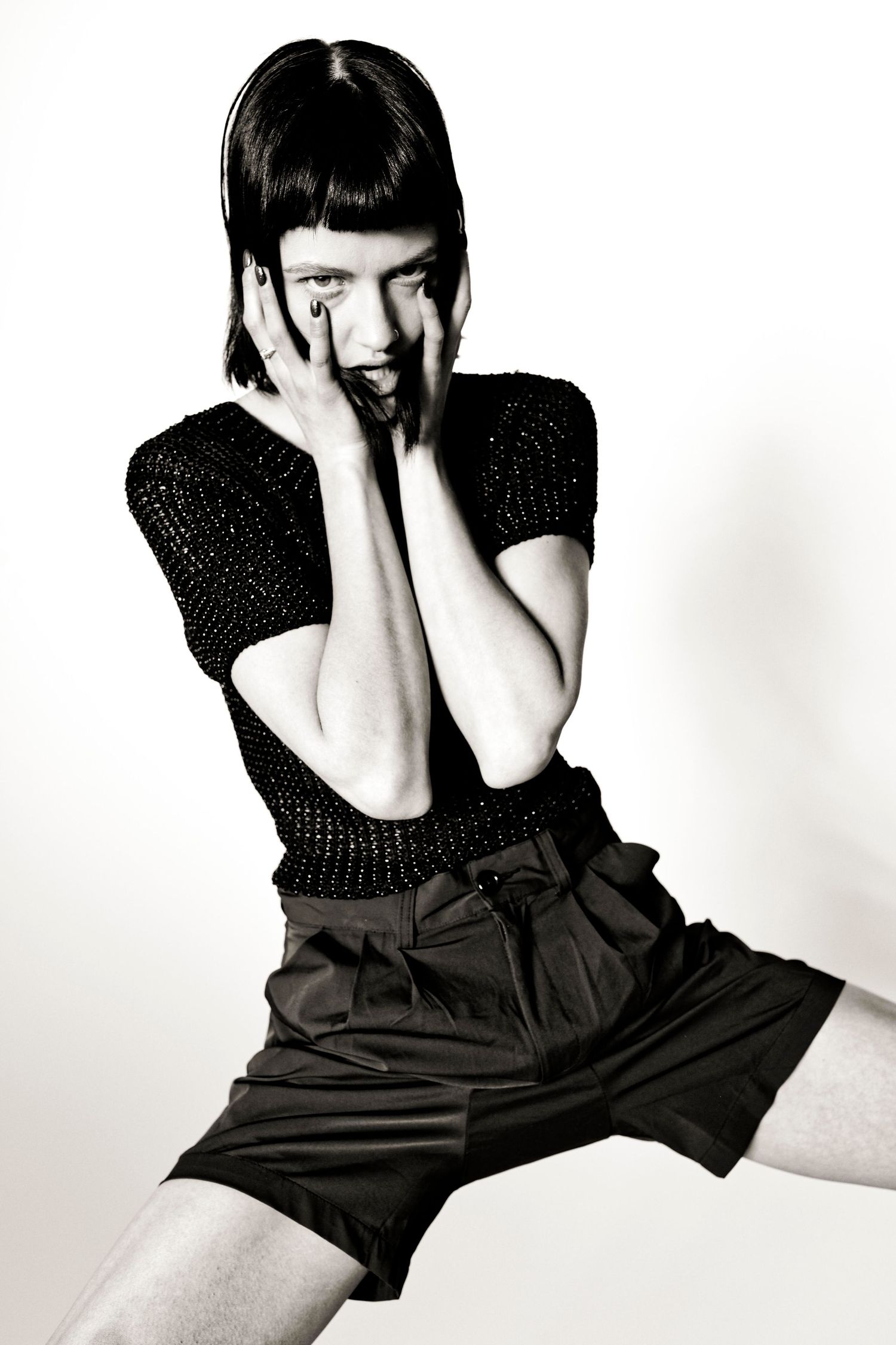 Black and white fashion photo of a woman in black shorts and top with hands framing her face.