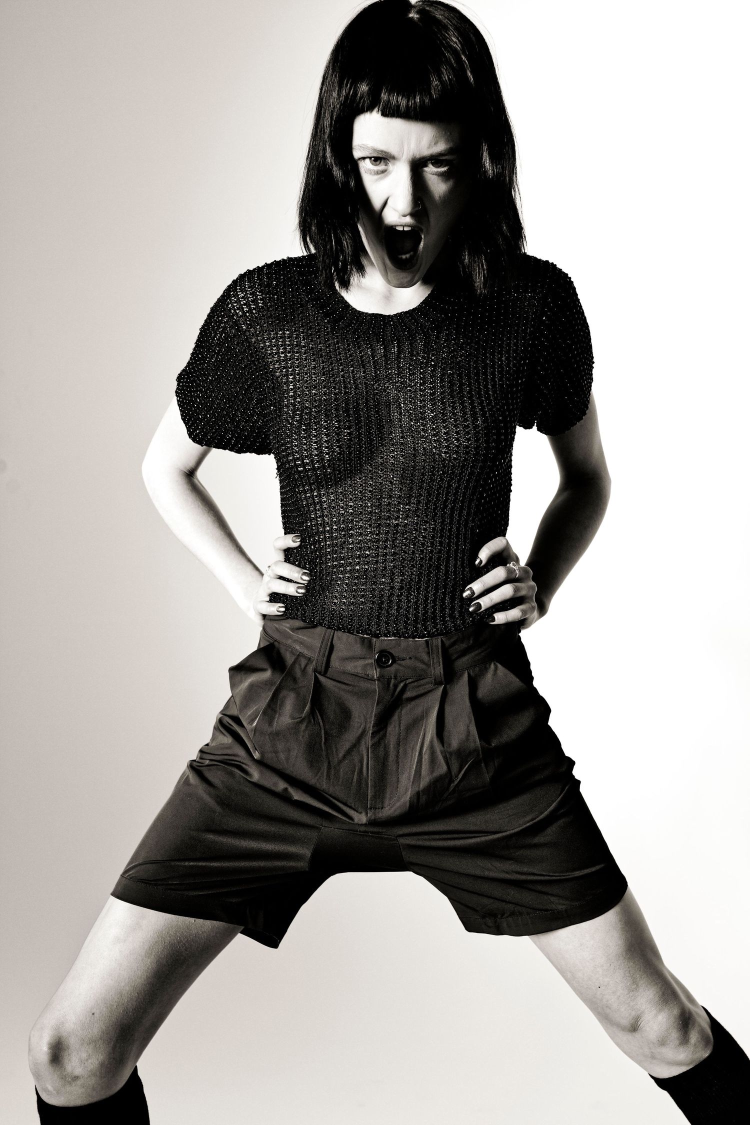 Person in black knit top and shorts striking a bold pose in a dramatic black and white fashion photo.