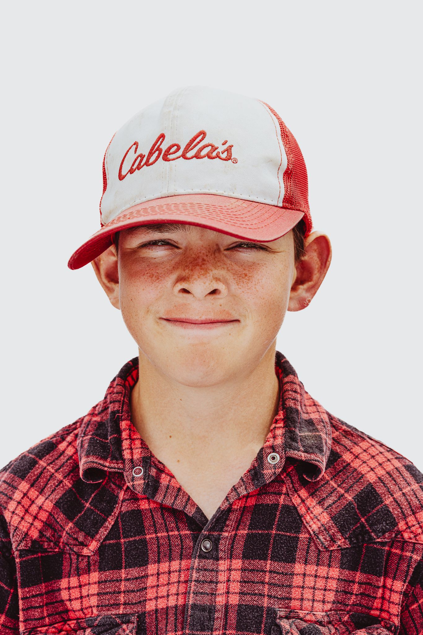Smiling freckled boy wearing a Cabelas baseball cap and red plaid flannel shirt, portrait photo.