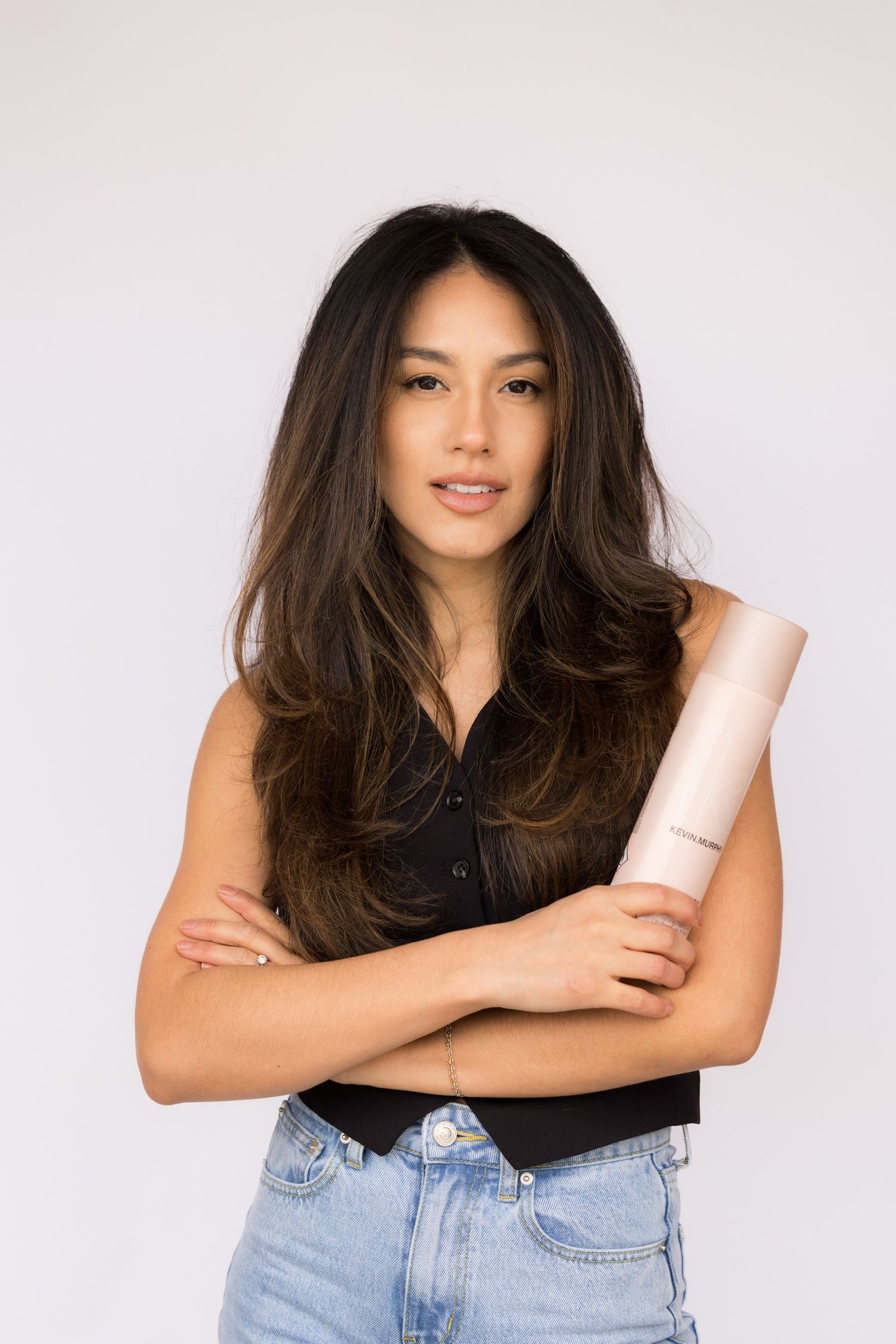 Woman with long dark hair holding a hair product bottle in studio.