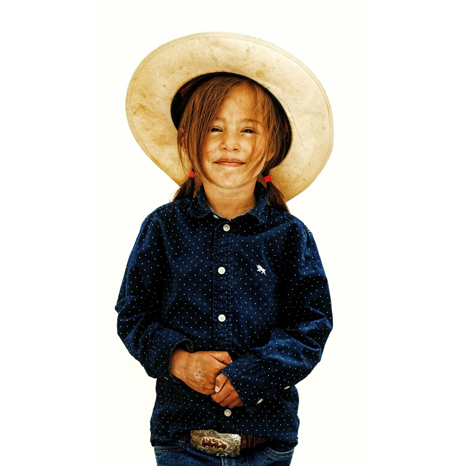 Adorable young child smiling in a large straw cowboy hat and dark western button-up shirt.