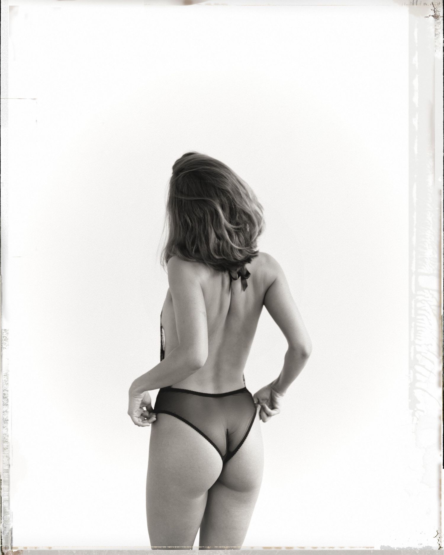Black and white photo of a woman in lingerie posing with her back to the camera.