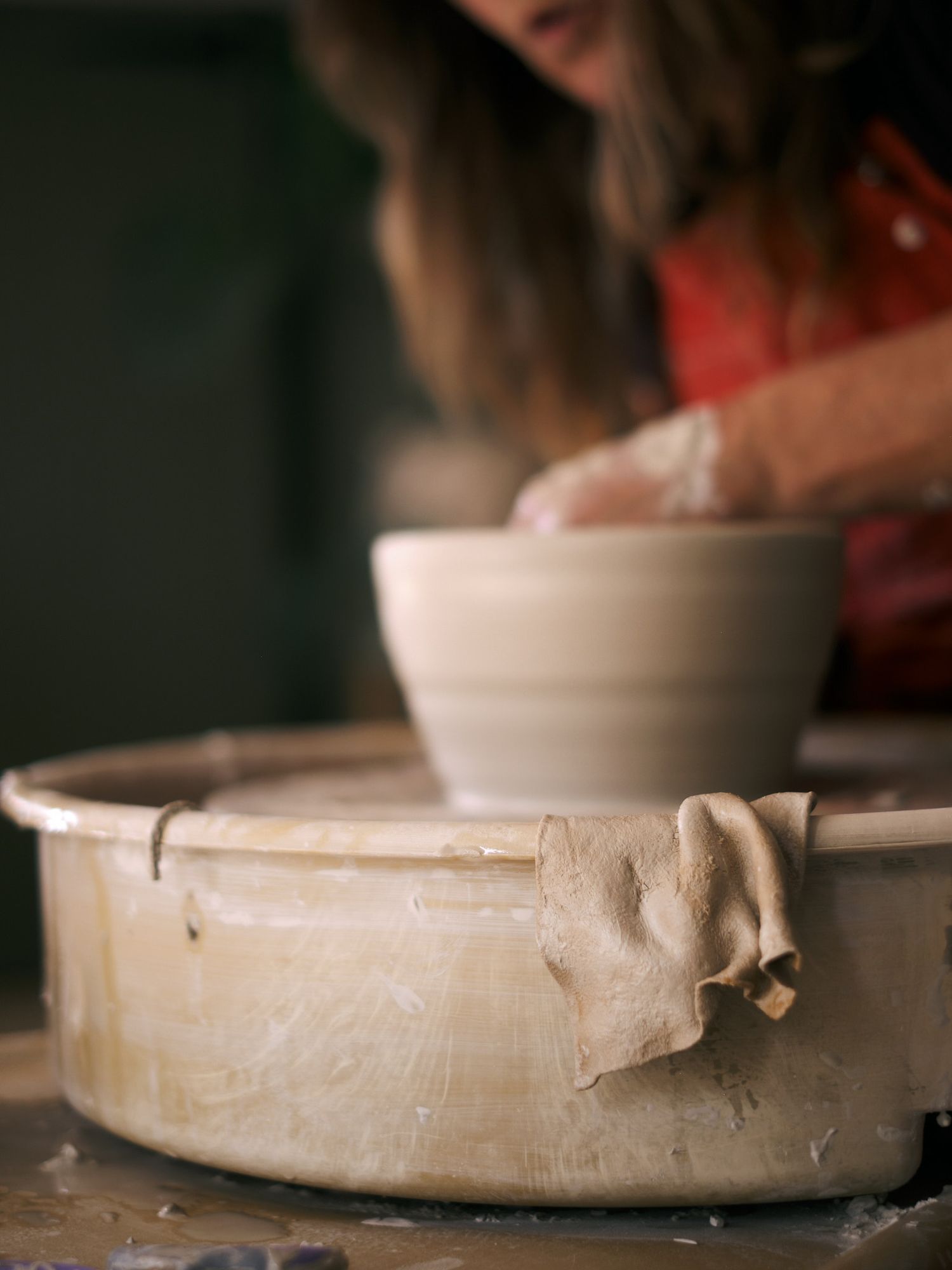 Female potter focused on throwing a white clay bowl on a spinning pottery wheel.