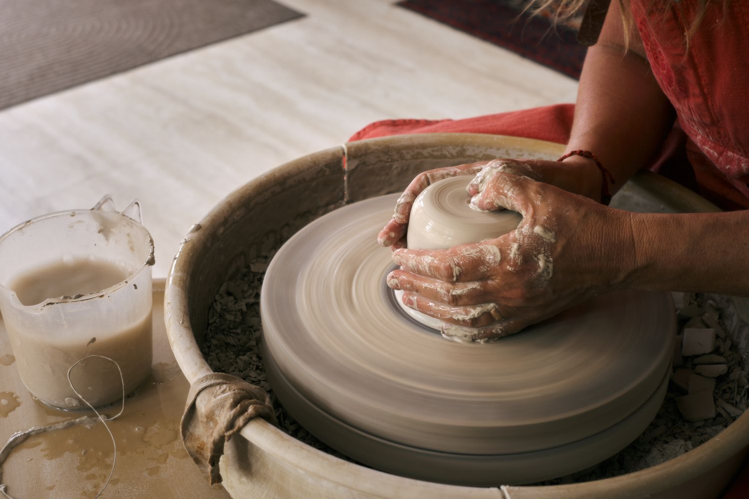 Top-down view of hands centering wet clay on a pottery wheel with slip water nearby.