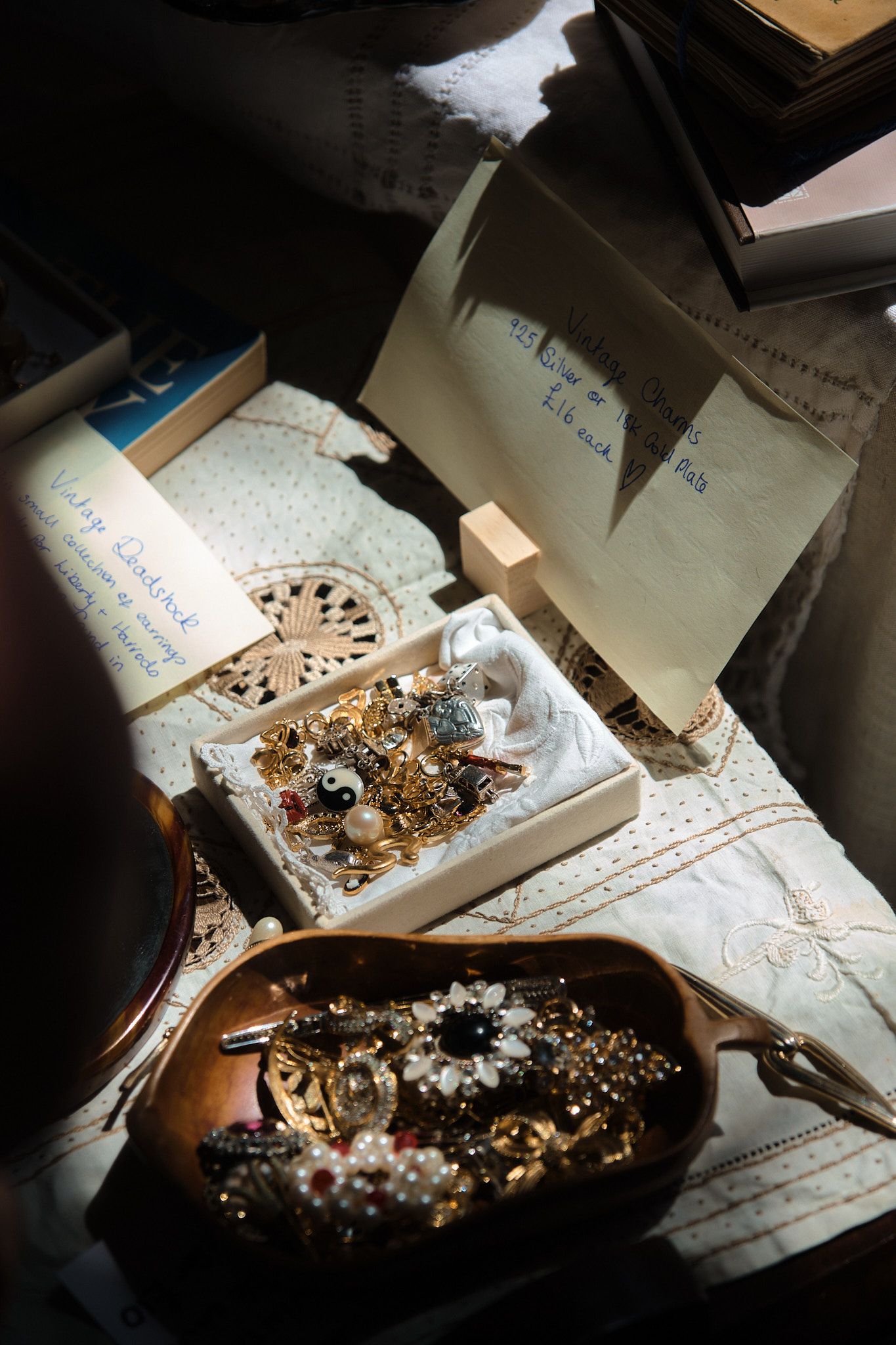 Vintage jewelry collection in wooden bowl and white box beside handwritten notes on embroidered tablecloth.