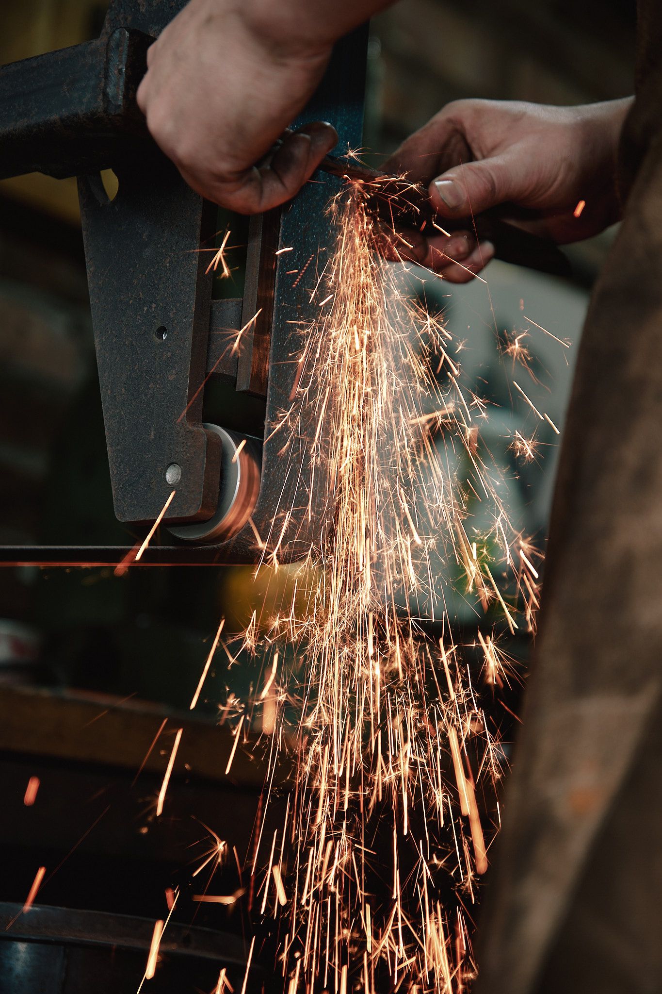 Worker grinding metal with an angle grinder, producing bright orange sparks flying in a dark workshop.