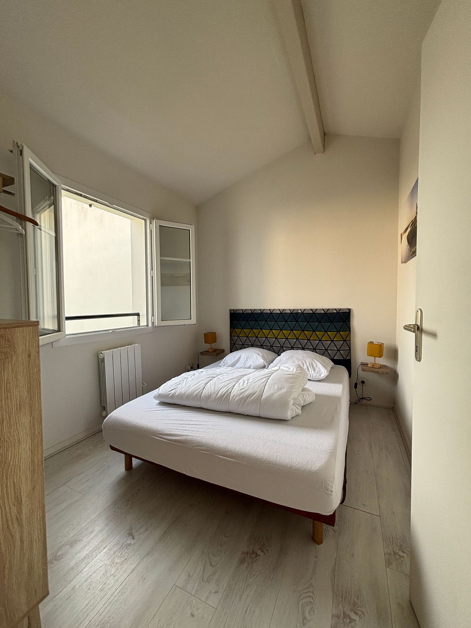 Chambre chaleureuse lumineuse avec lit double, tête de lit à motifs et parquet en bois blanc