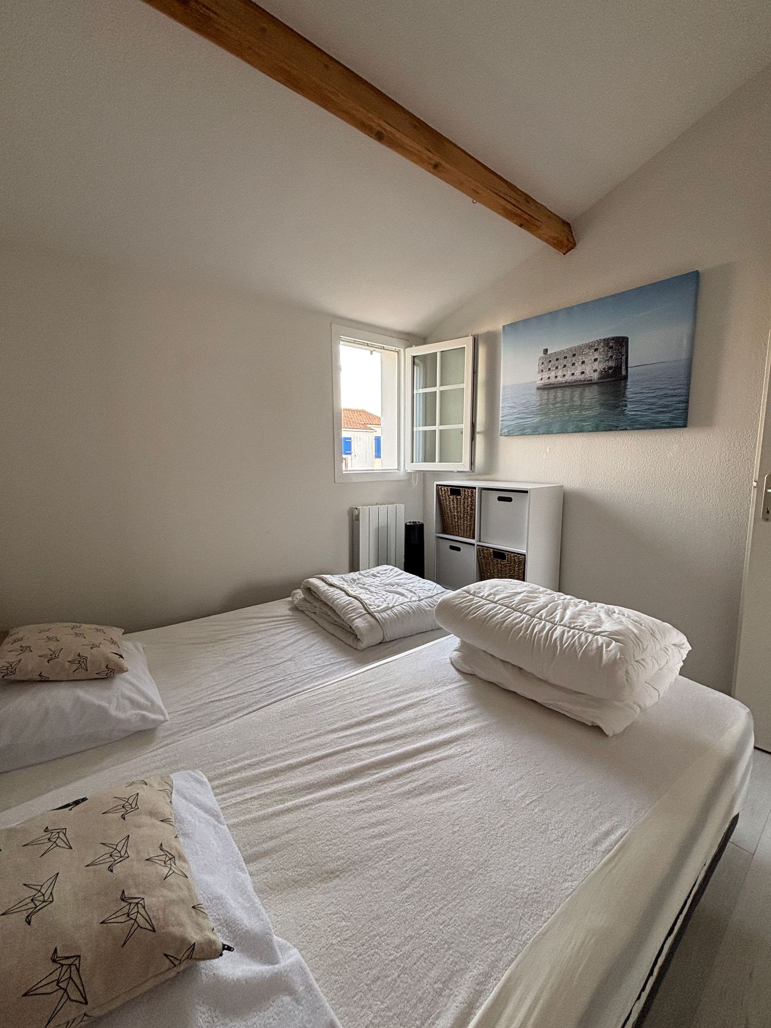 Chambre lumineuse à deux lits simples, poutre apparente et tableau de Fort Boyard