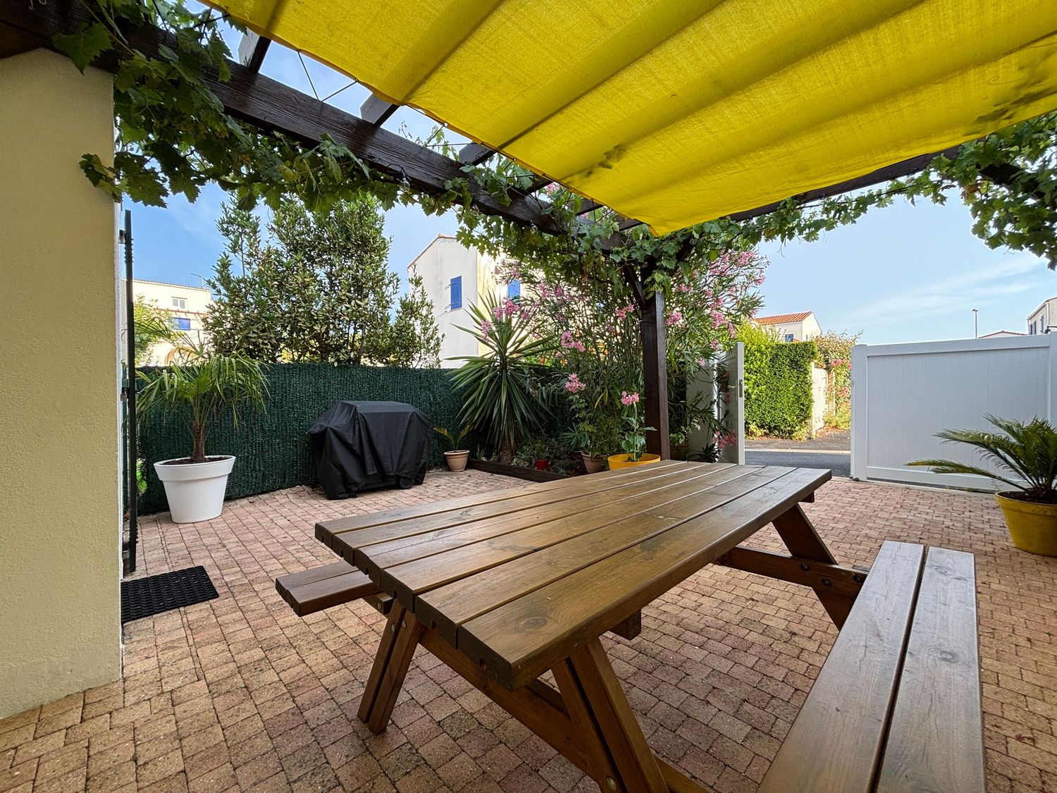 Terrasse extérieure avec table en bois sous une pergola végétalisée et jardin fleuri