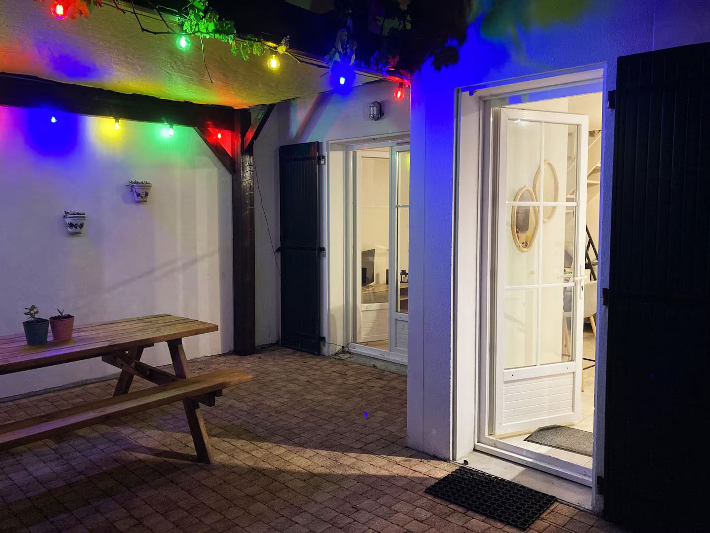 Terrasse illuminée de guirlandes la nuit, table et portes-fenêtres ouvertes sur le salon de la maison de Fouras