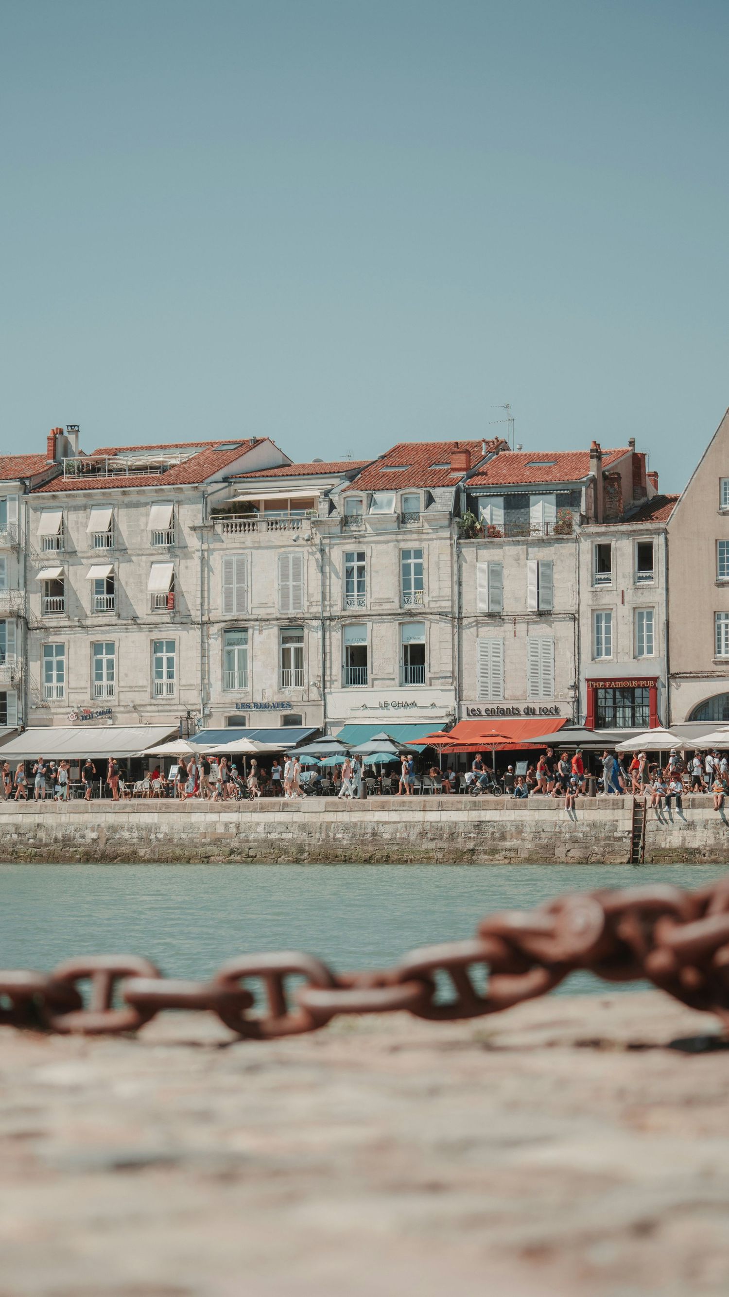 Promenade animée en bord de mer, façades anciennes et commerces sous le soleil de la Rochelle