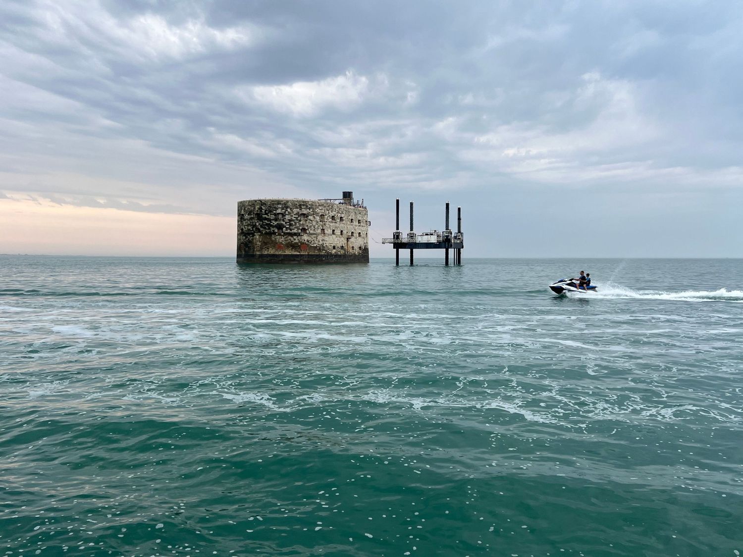 Fort Boyard émergeant d'une mer turquoise, un jet-ski passant au premier plan