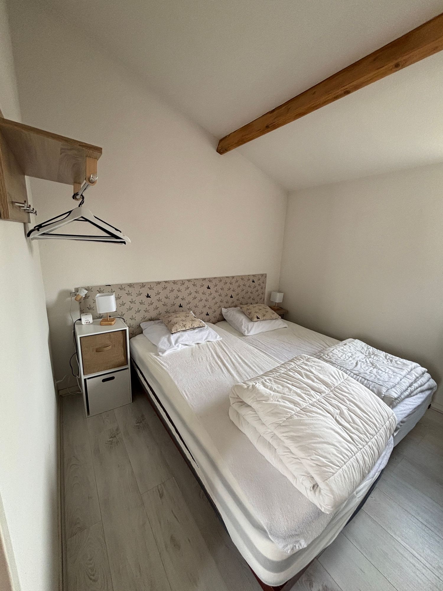 Chambre claire avec lit double, linge blanc, poutre apparente et parquet clair
