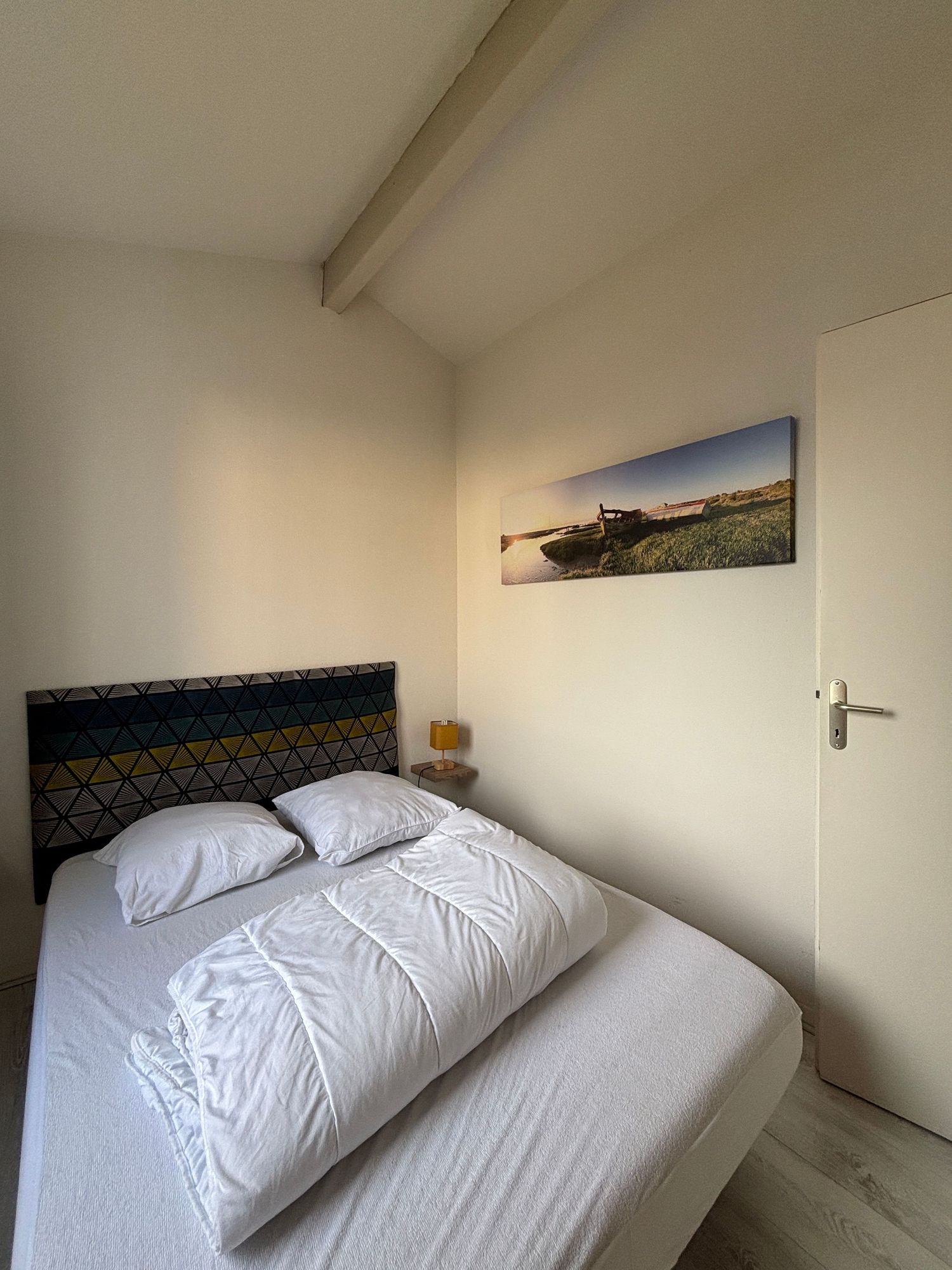 Chambre avec lit double, linge blanc, poutre apparente et décoration marine