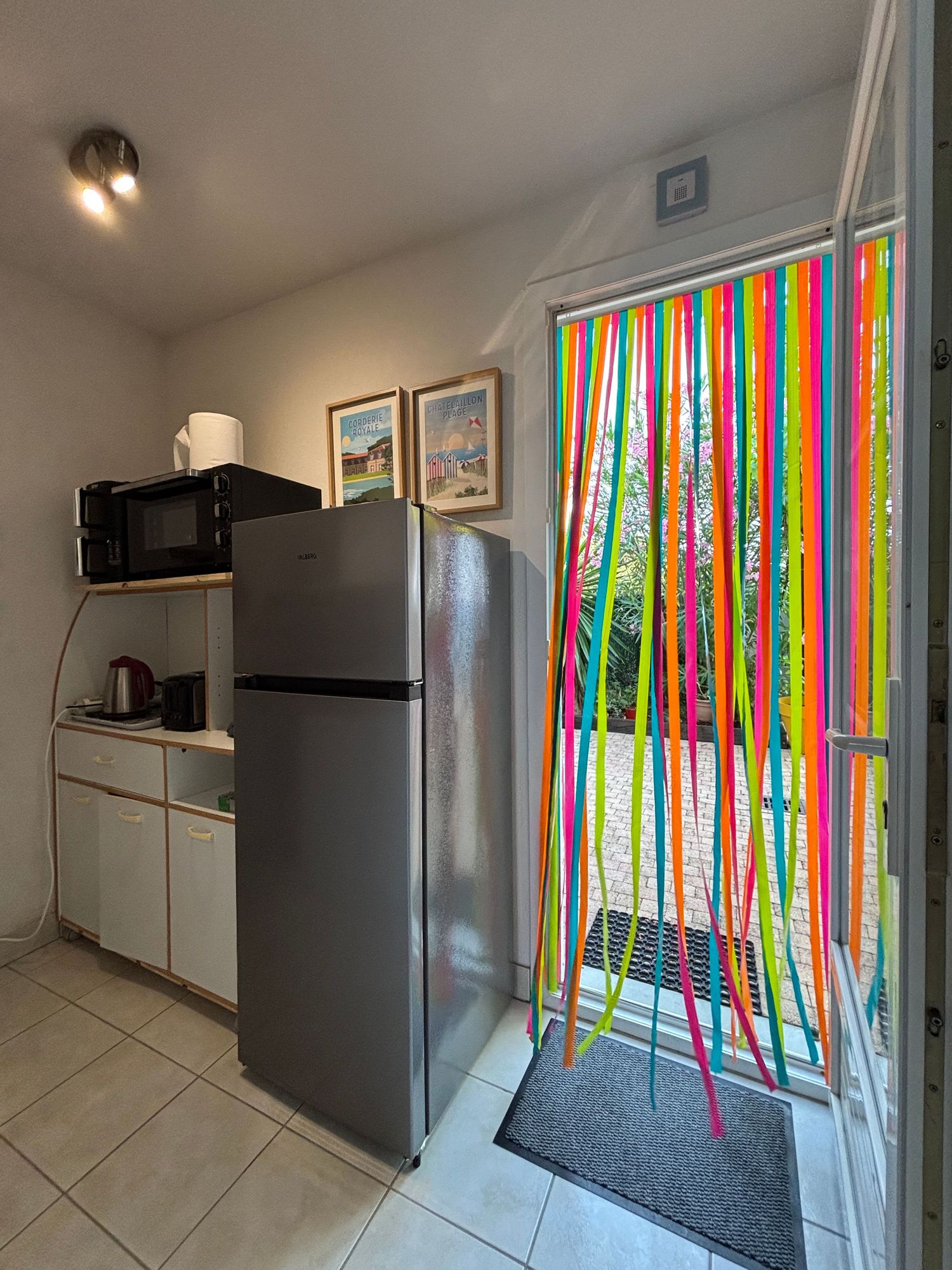 Coin cuisine avec réfrigérateur, micro-ondes et rideau de porte à lanières colorées
