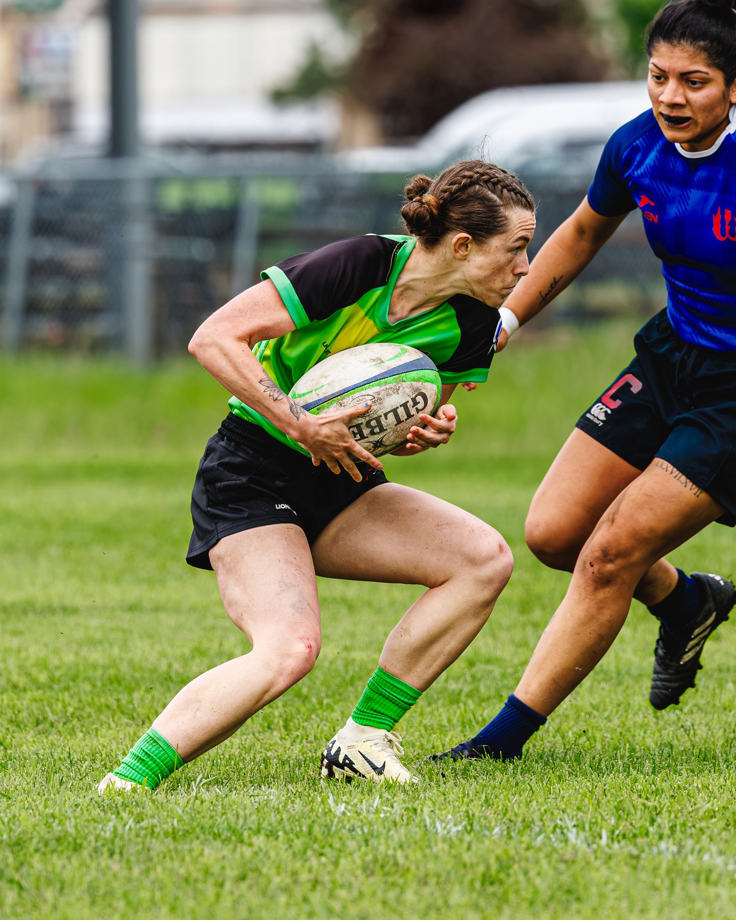 Women's rugby player drives forward with Gilbert ball while opponent attempts tackle.