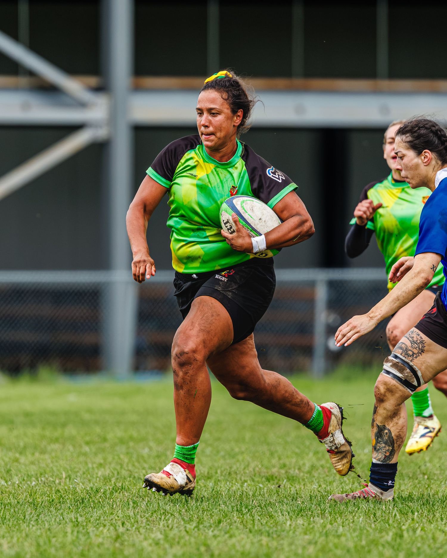 Female rugby player in green and black jersey runs with ball in women's rugby game.