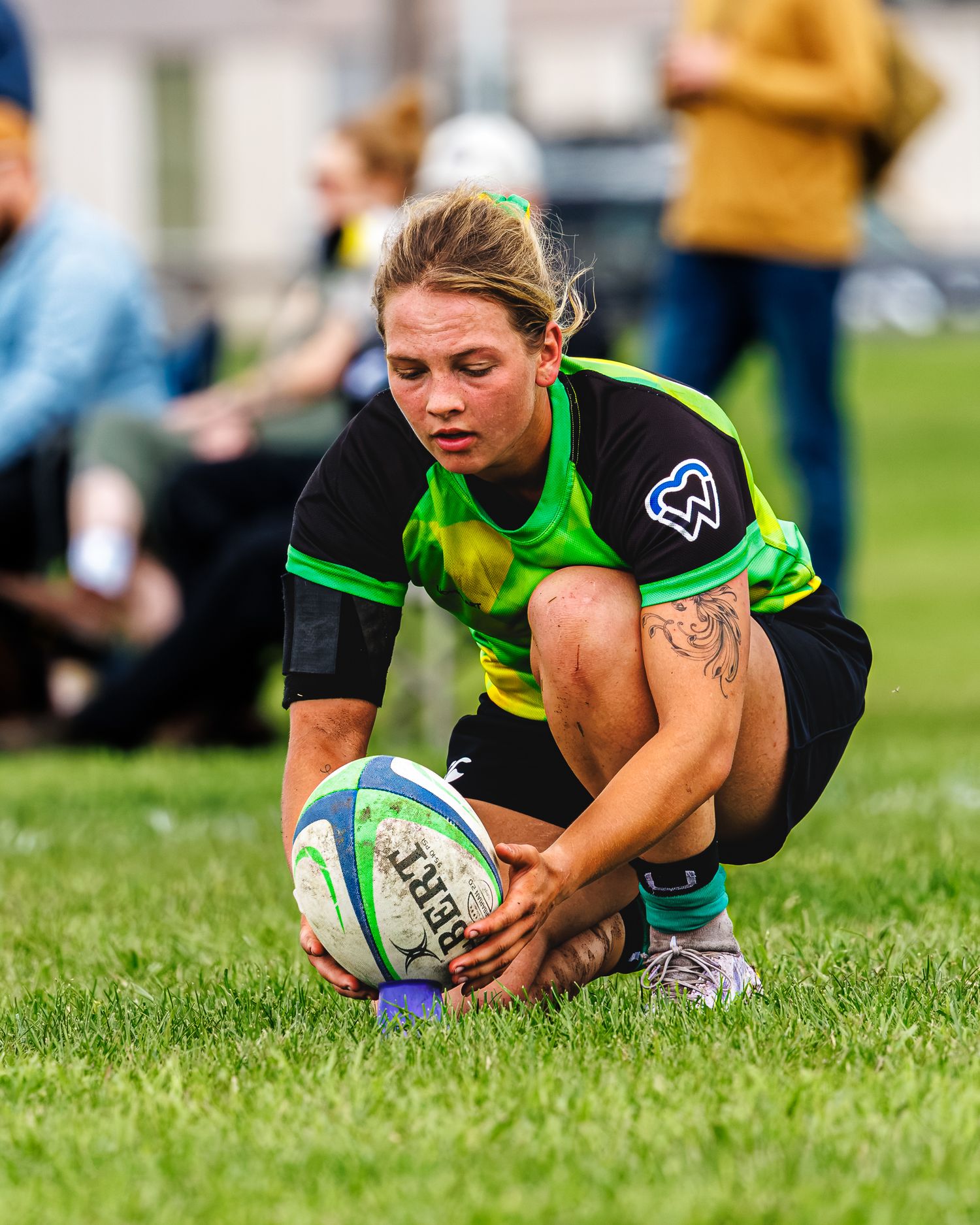 Female rugby player crouches to pick up rugby ball during women's outdoor match.