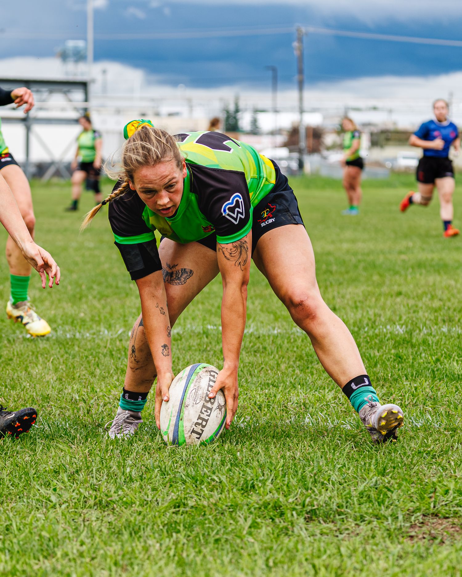 Tattooed female rugby player scores try, placing ball on grass during women's rugby match.