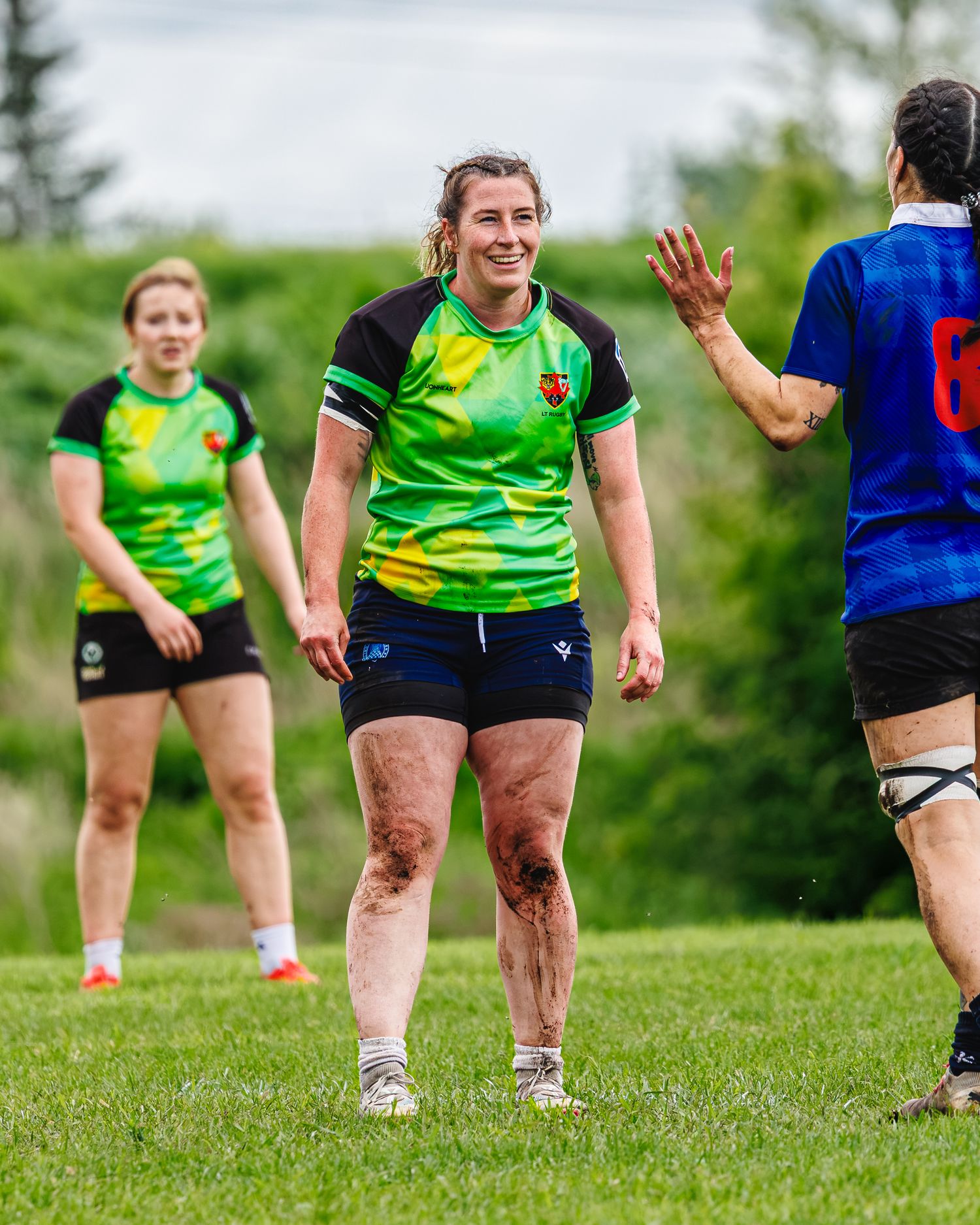 Smiling female rugby player in green jersey gives high five after muddy match outdoors.