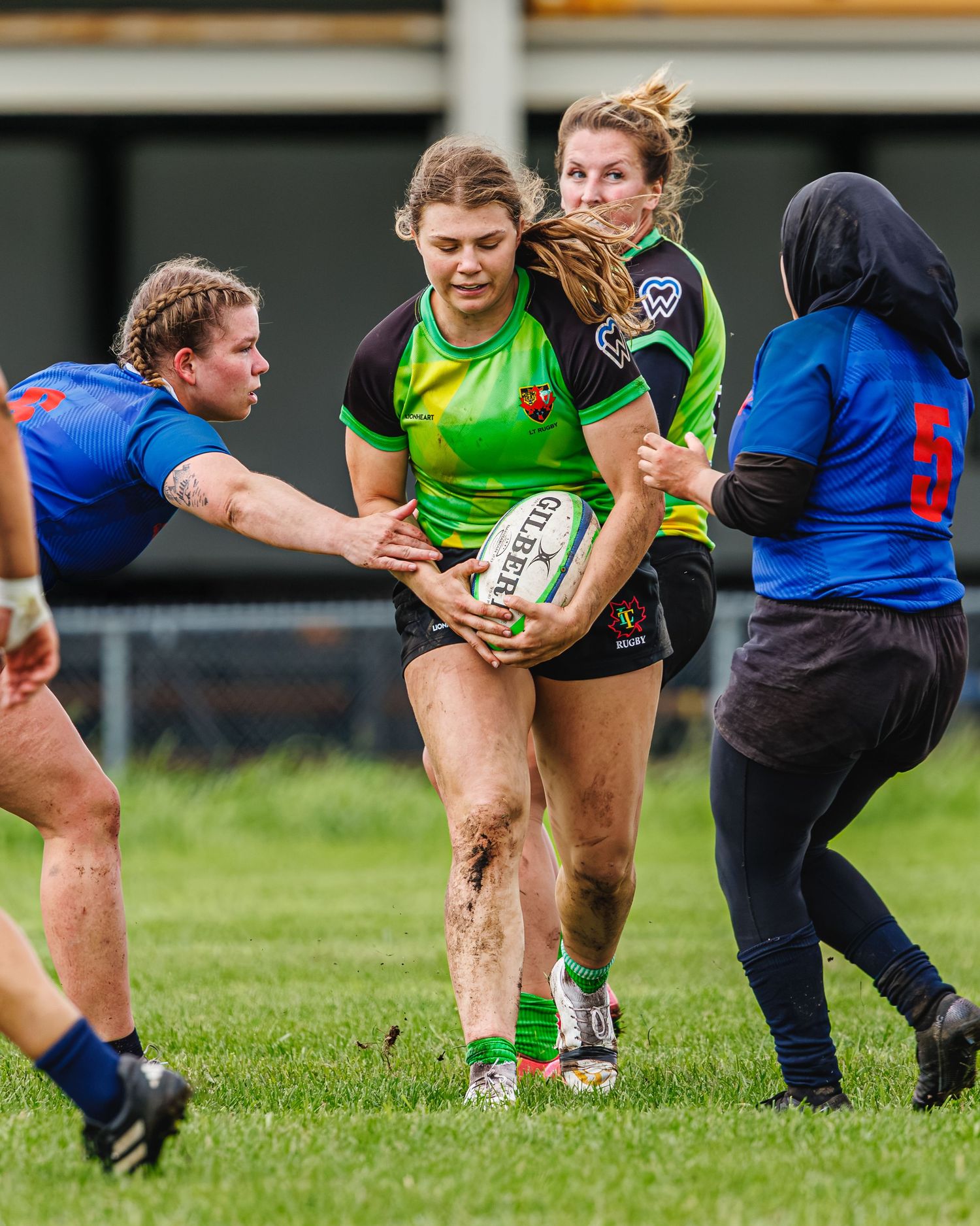 Female rugby player powers through defenders carrying ball in muddy women's rugby game.